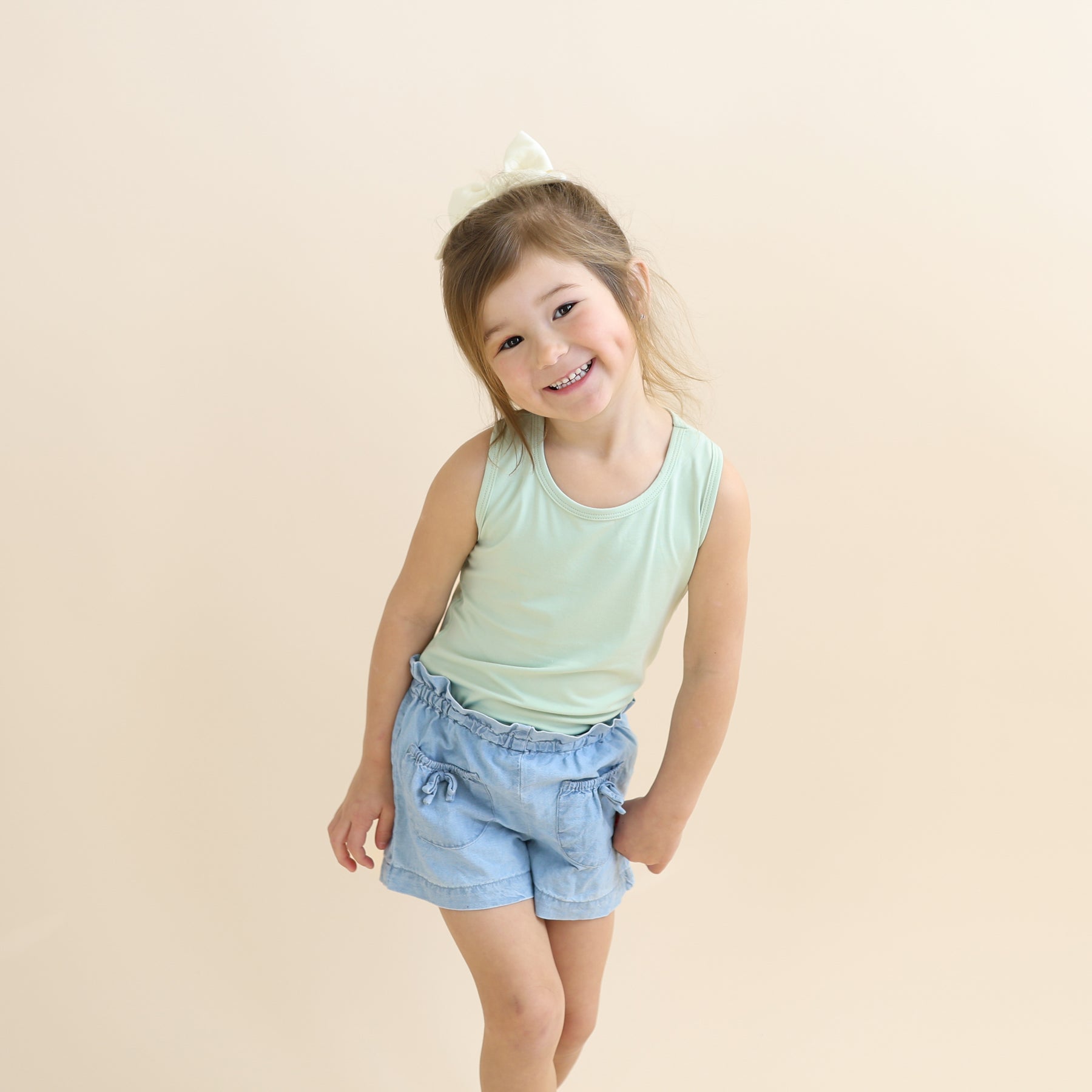 Young girl posing wearing the Toddler Tank Top in Basil with jean shorts