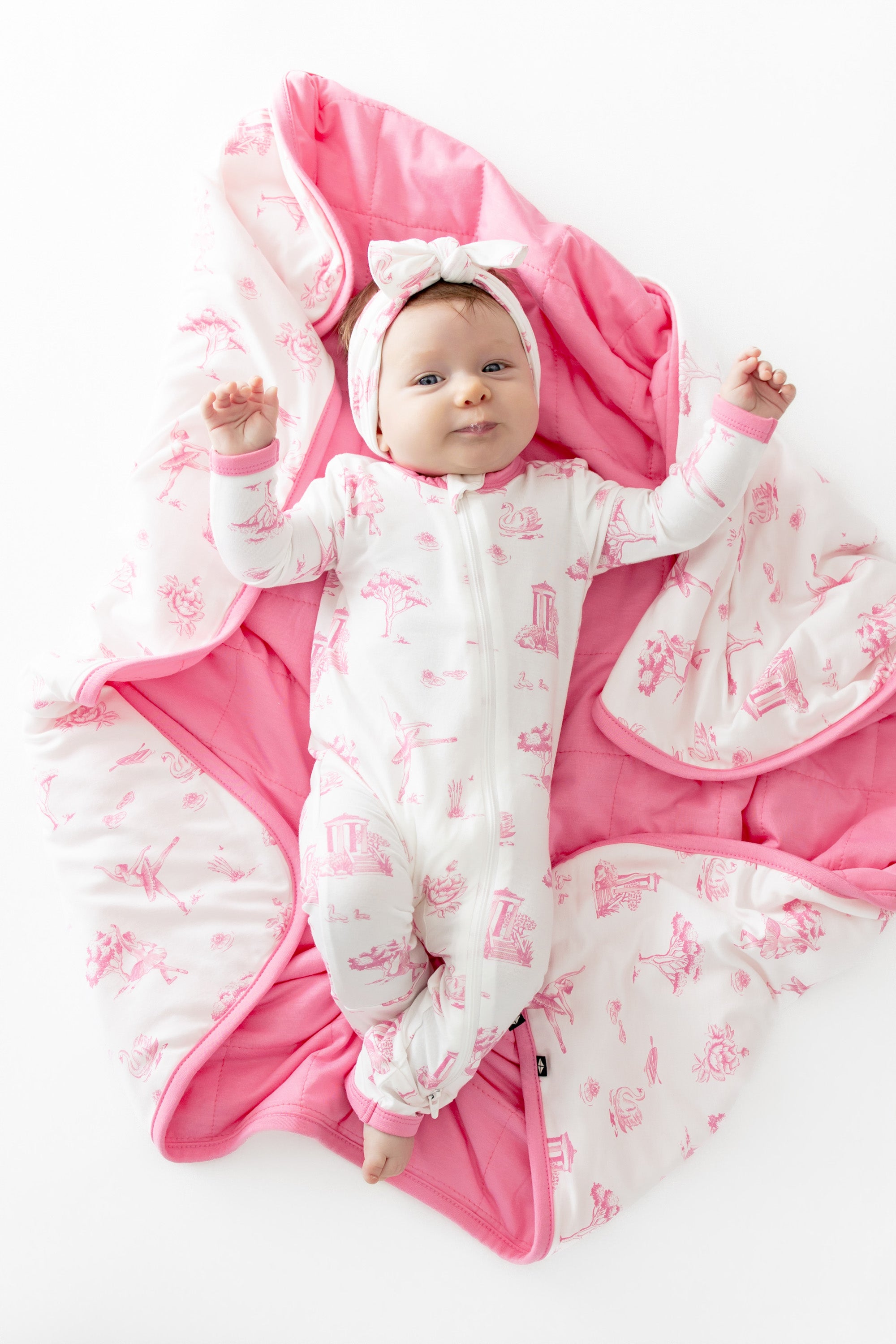 Infant laying on a Baby Blanket in Toile Ballet wearing a matching zippered romper