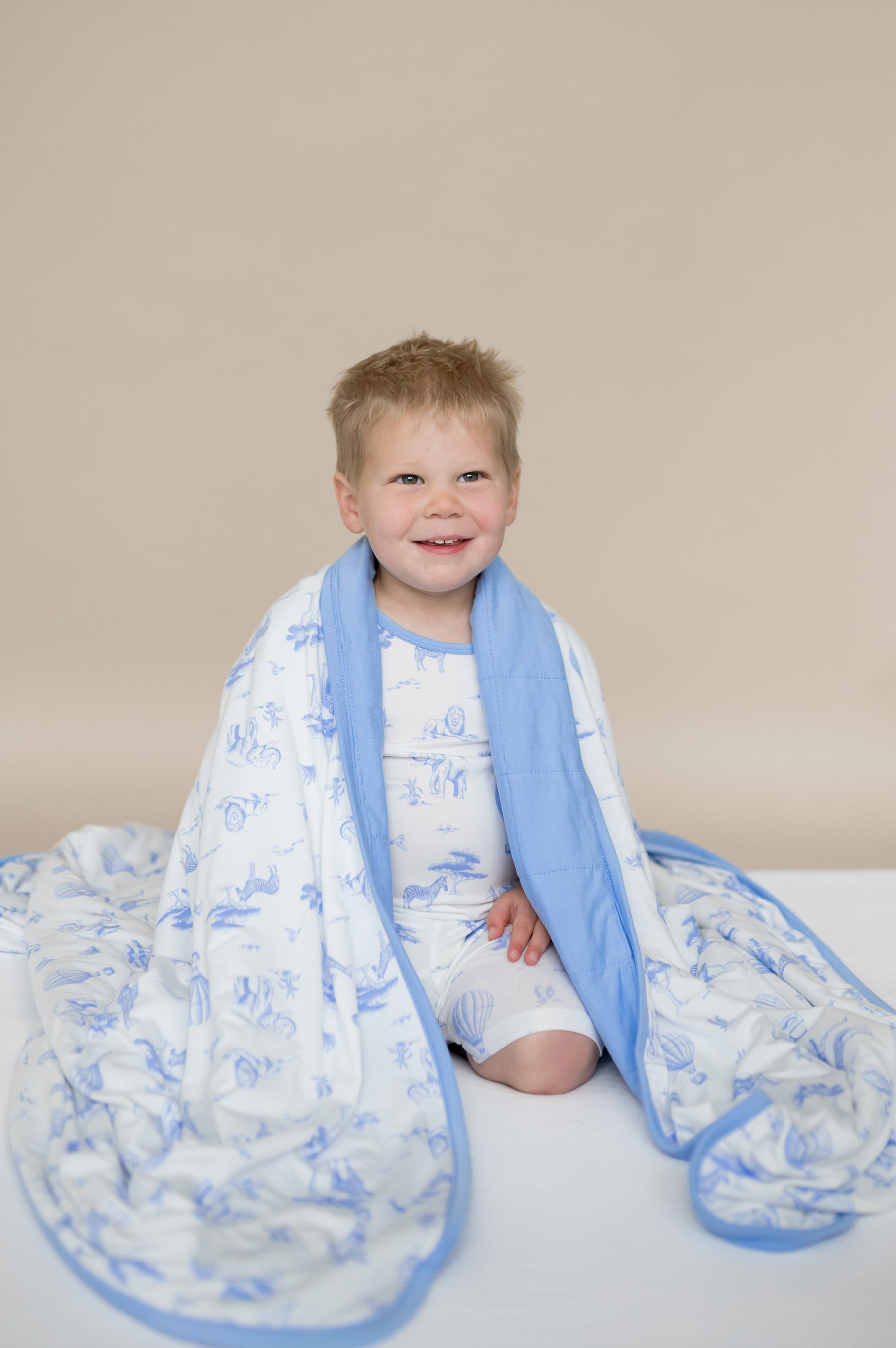Young boy sitting on his knees with the Youth Blanket in Toile Safari 1.0 around his shoulders