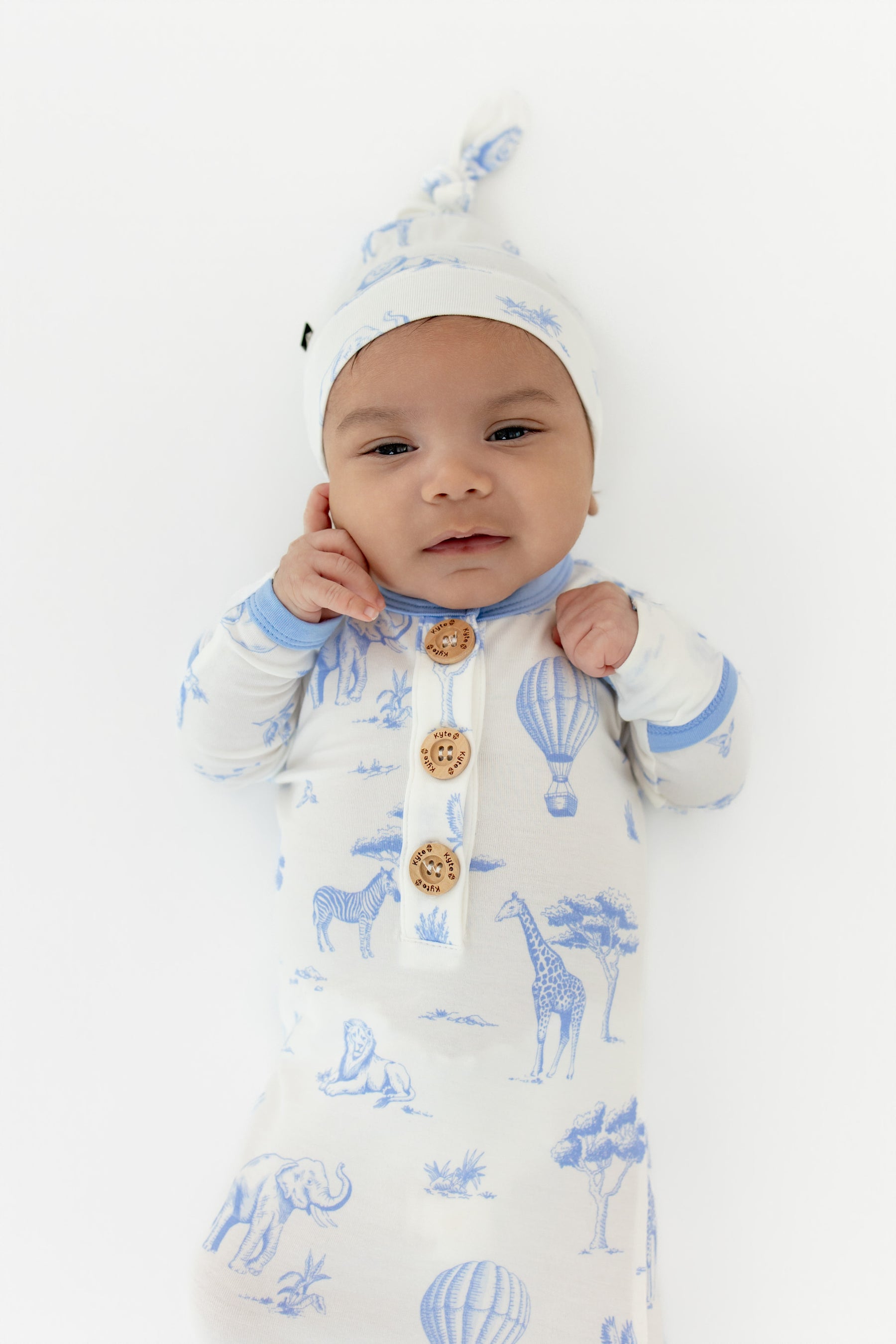 Close up of infant wearing the Knotted Gown with Hat Set in Toile Safari showing the Kyte Baby engraved wooden buttons
