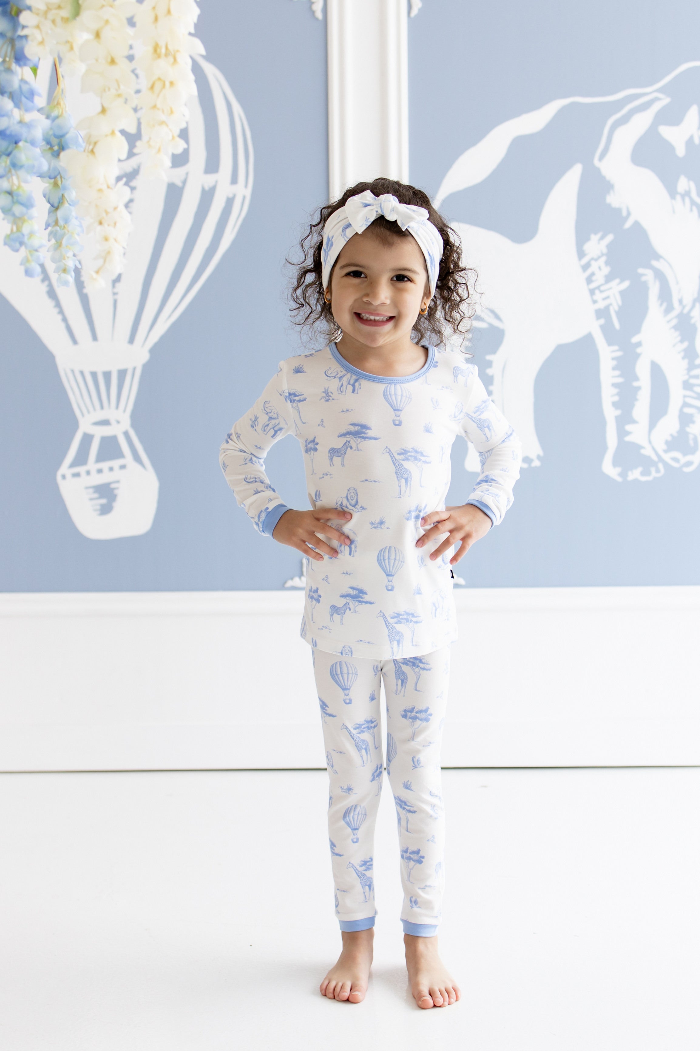 Young girl wearing the Long Sleeve Pajamas in Toile Safari posing in front of white and blue safari themed paintings