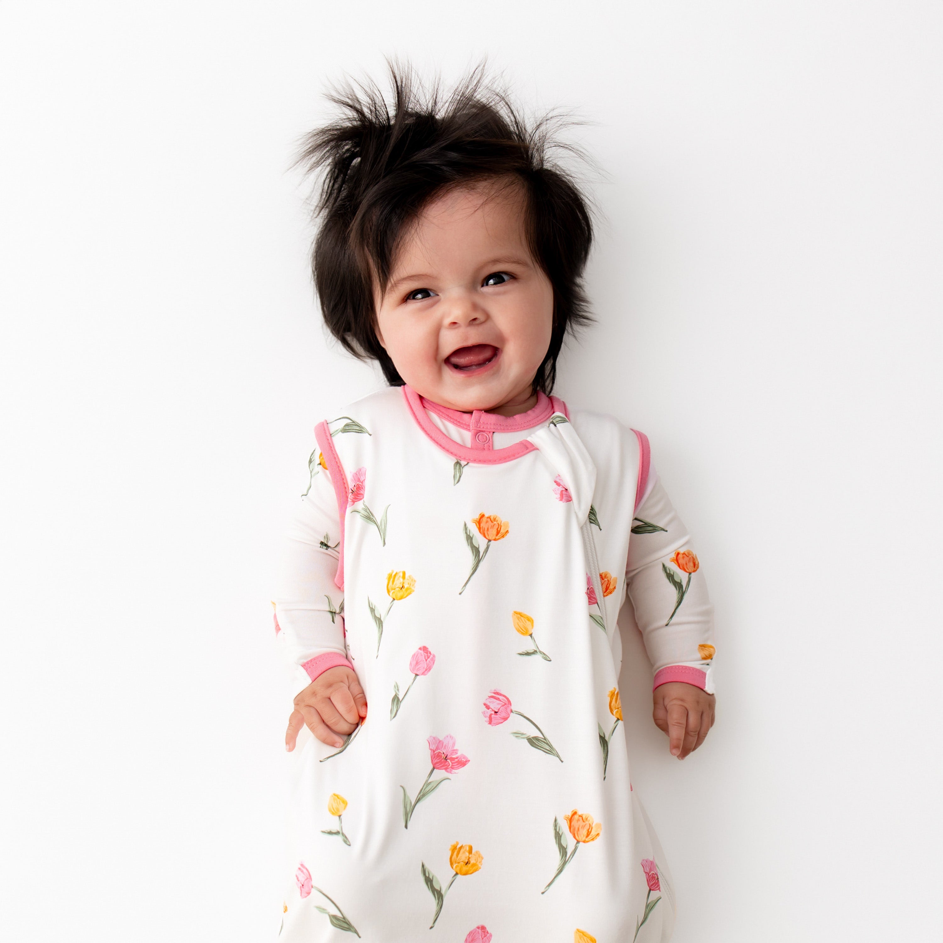 Close up of smiling toddler wearing the Sleep Bag in Tulip 0.5 with a matching long sleeve romper on underneath