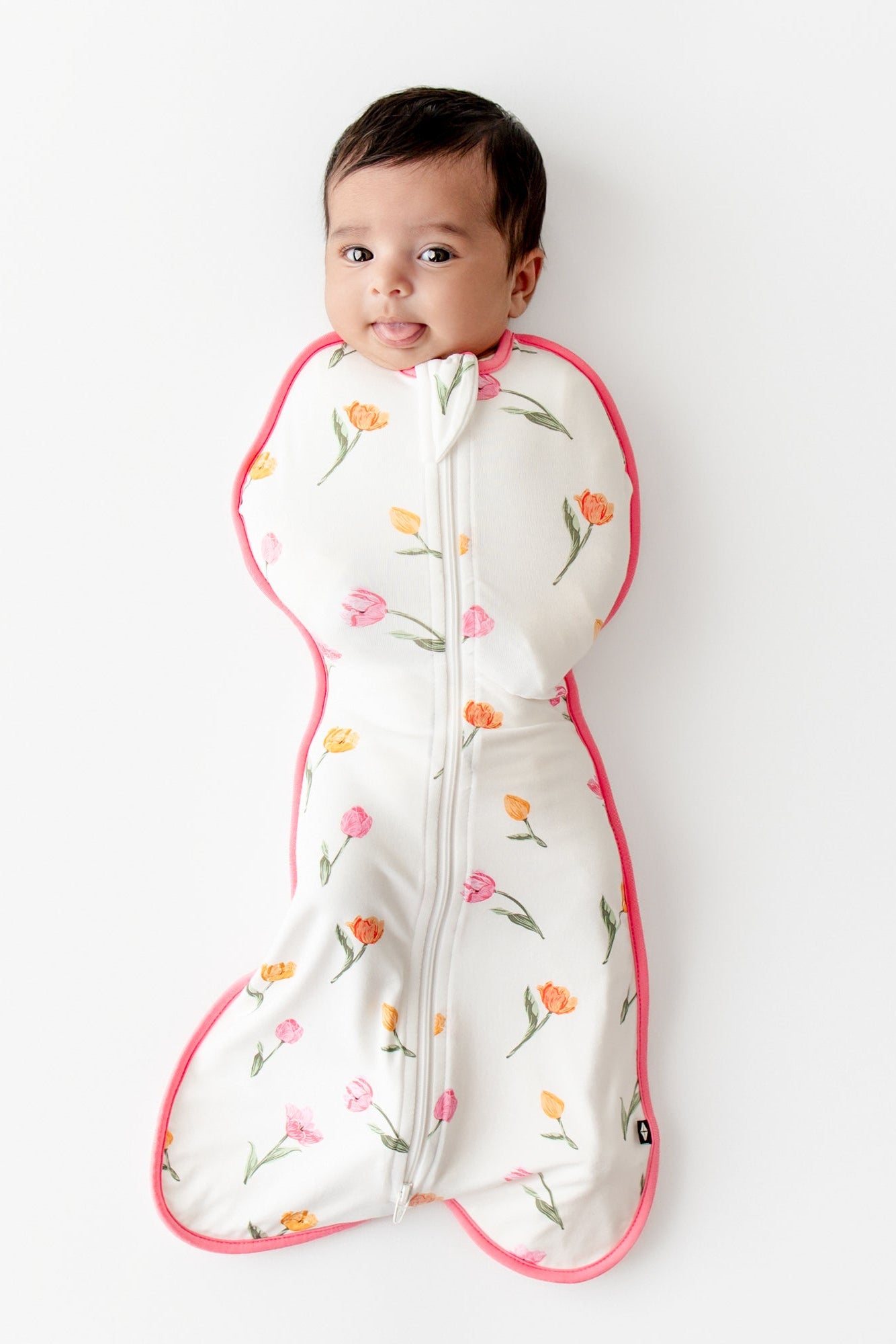 Newborn laying on a white surface with her tongue sticking out wearing the Swaddle Bag in Tulip 0.5