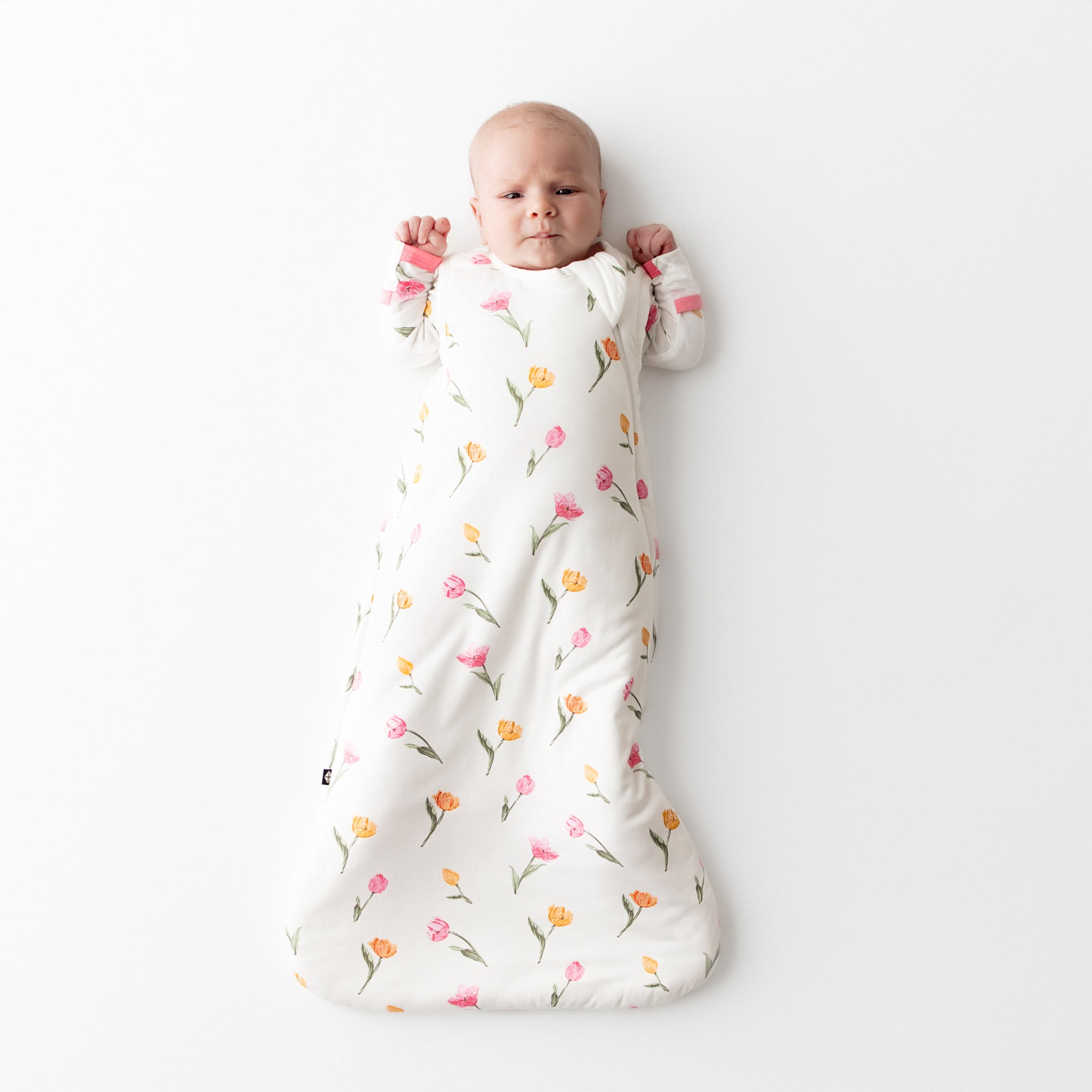 Infant laying on a white surface wearing the Sleep Bag in Tulip 1.0 with matching romper on underneath