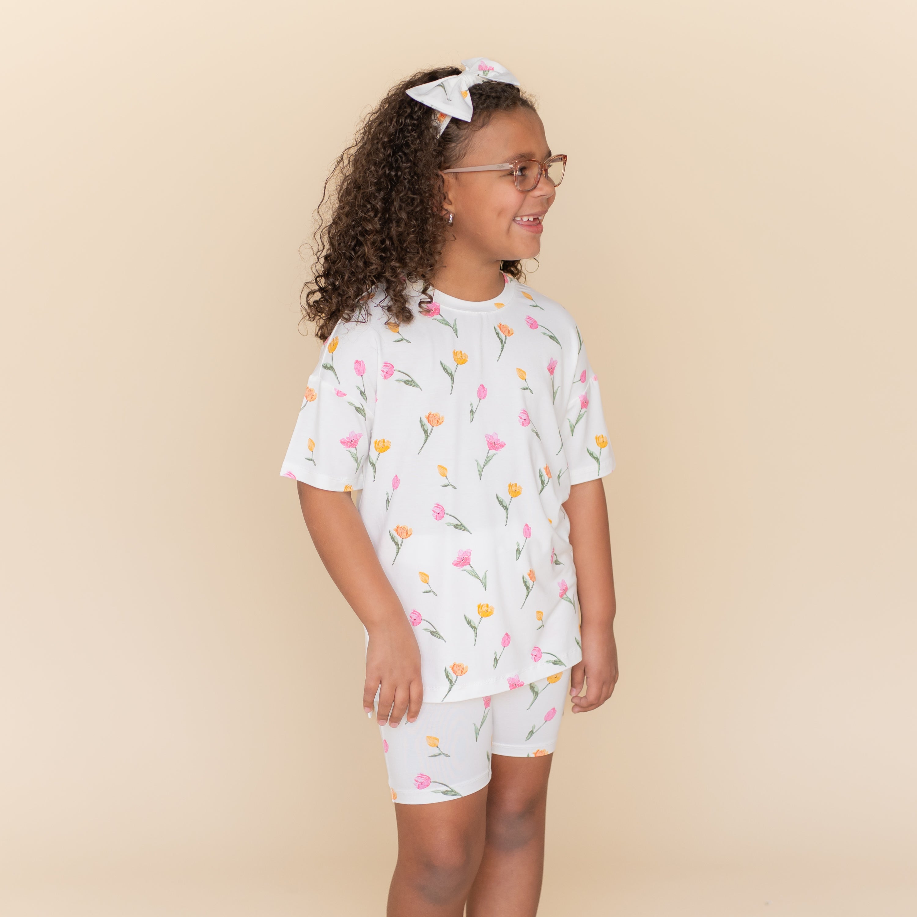 Young smiling girl wearing the Toddler Biker Short Set in Tulip looking off to the side standing in front of a light neutral background