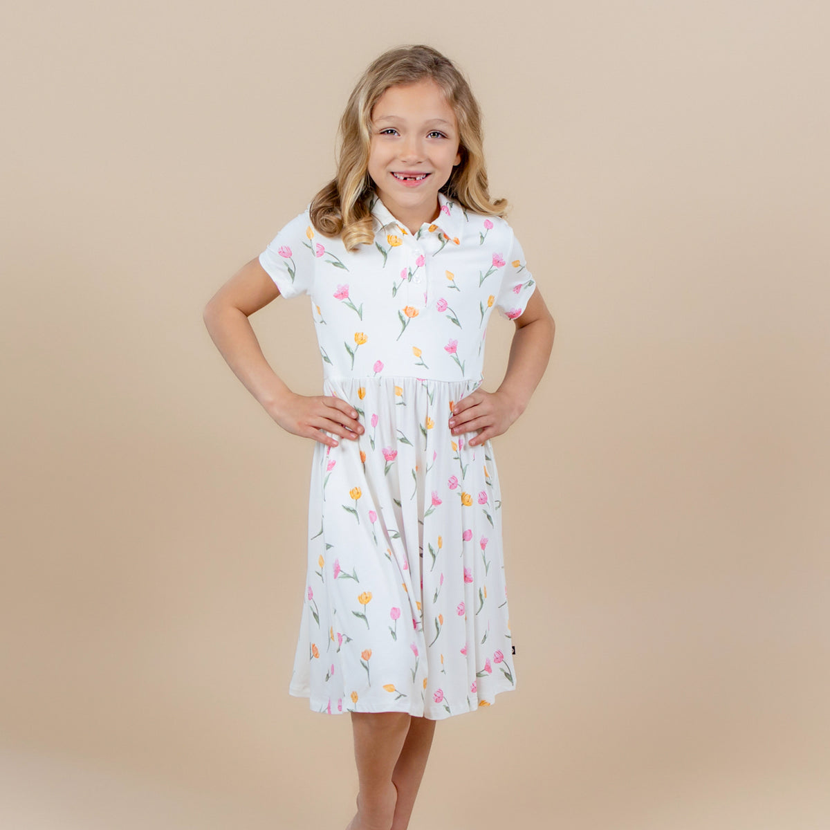 Young girl posing wearing the Polo Dress in Tulip in front of a light neutral background