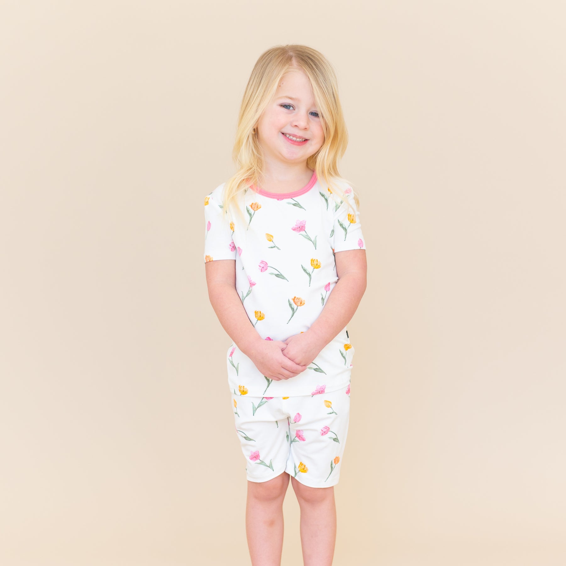 Young girl standing in front of a light taupe background wearing the Short Sleeve Pajamas in Tulip with her hands folded in front of her