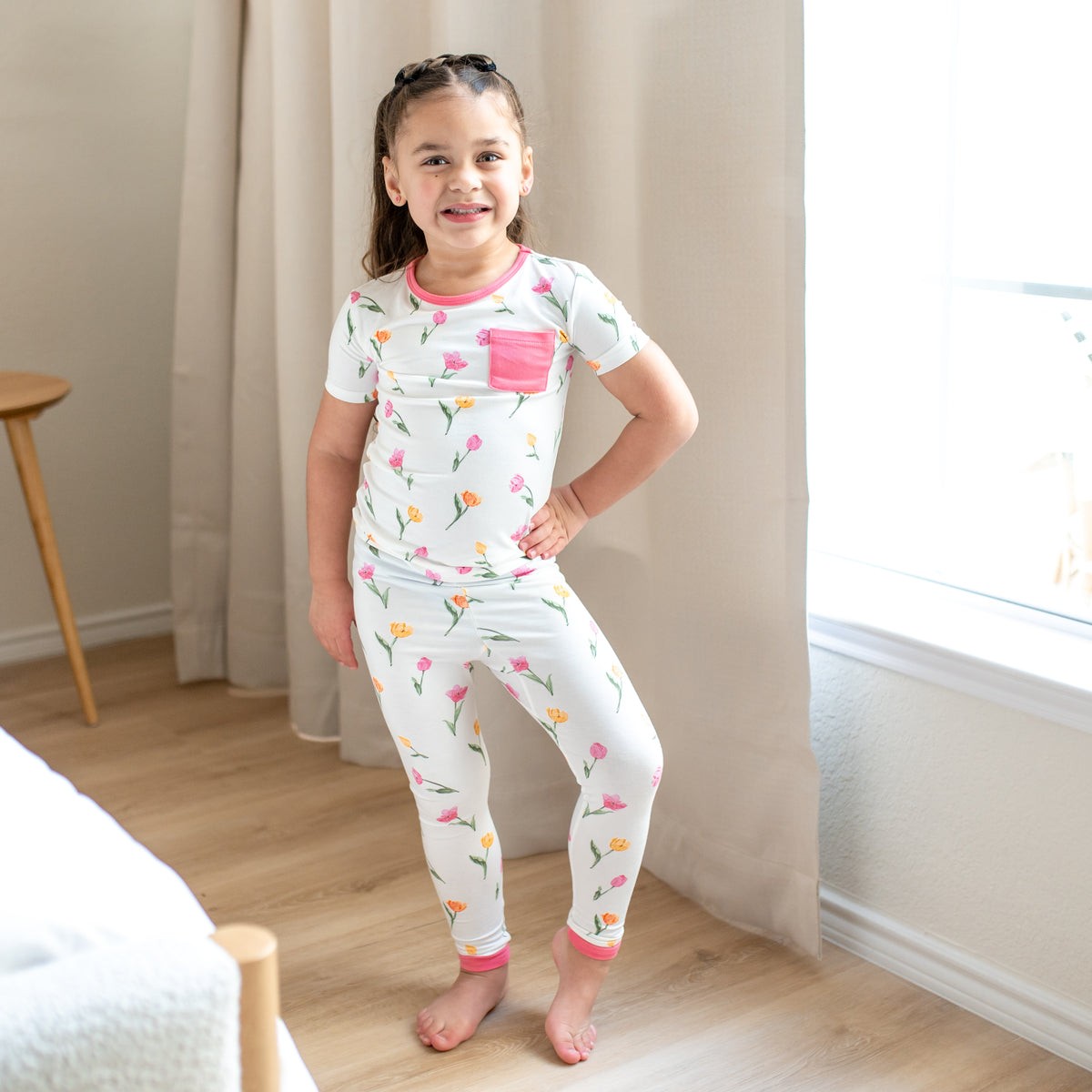 Young girl posing wearing the Short Sleeve with Pants Pajamas in Tulip standing beside a window 