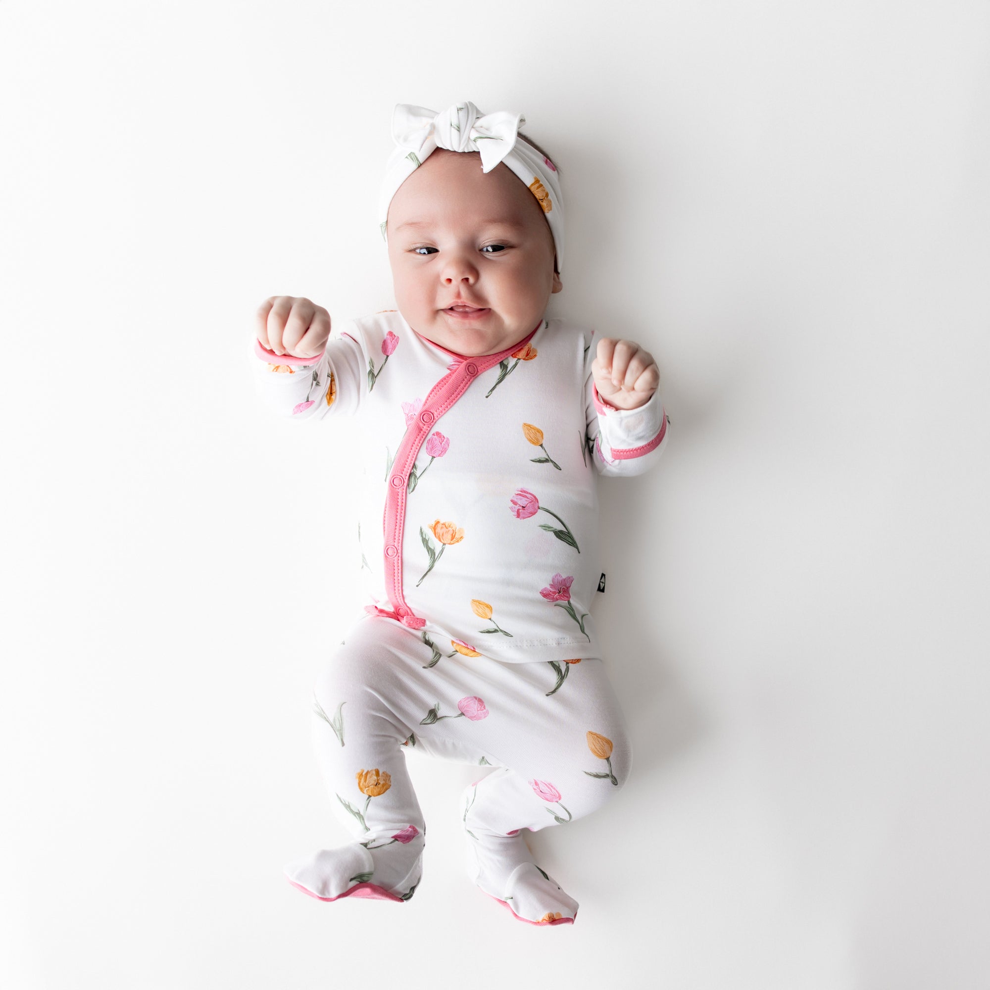 Newborn laying on a white surface wearing the Take Me Home Set with Bow in Tulip