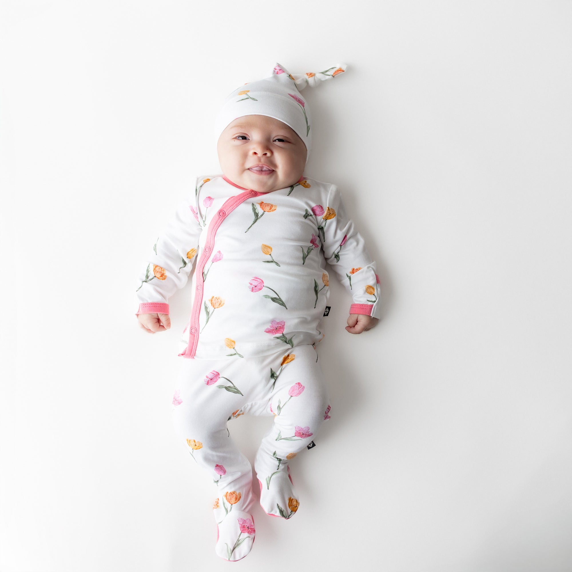 Newborn laying on a white surface wearing the Take Me Home Set with Cap in Tulip