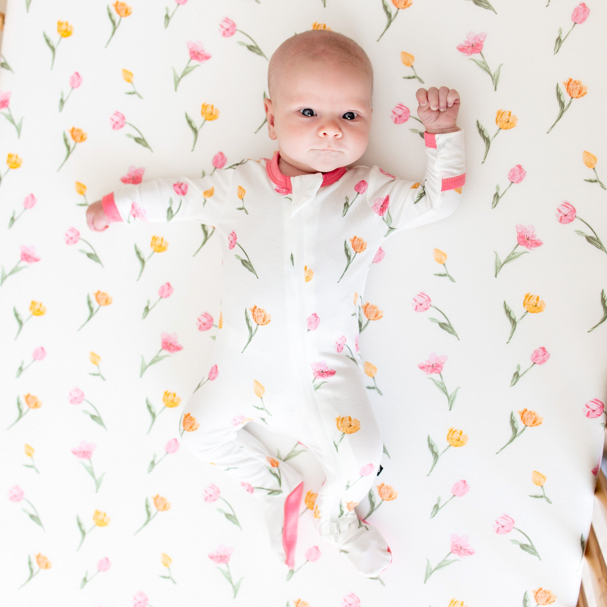 Infant laying in a crib on a Crib Sheet in Tulip wearing a matching zippered footie