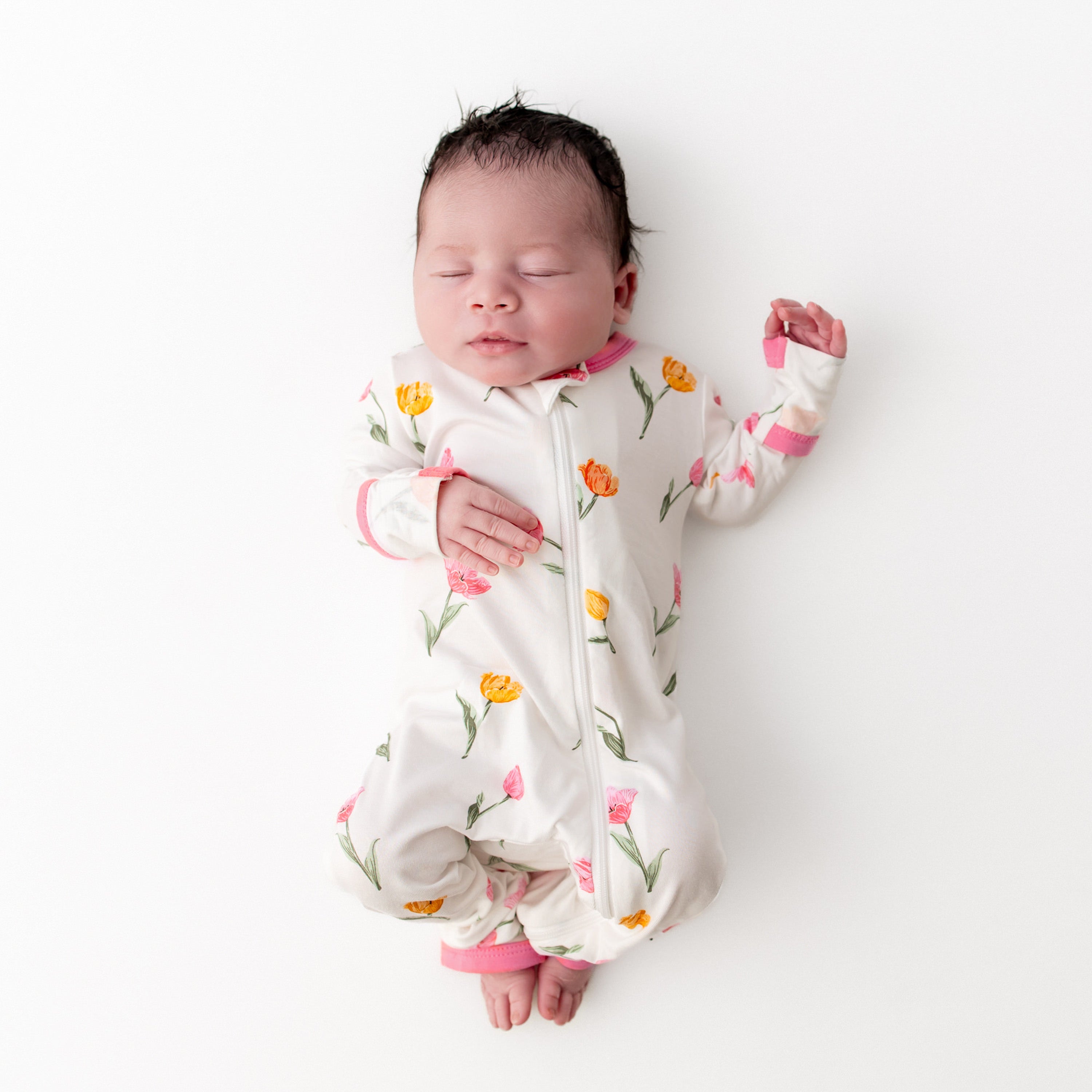 Sleeping newborn laying on a white surface wearing the Zippered Romper in Tulip