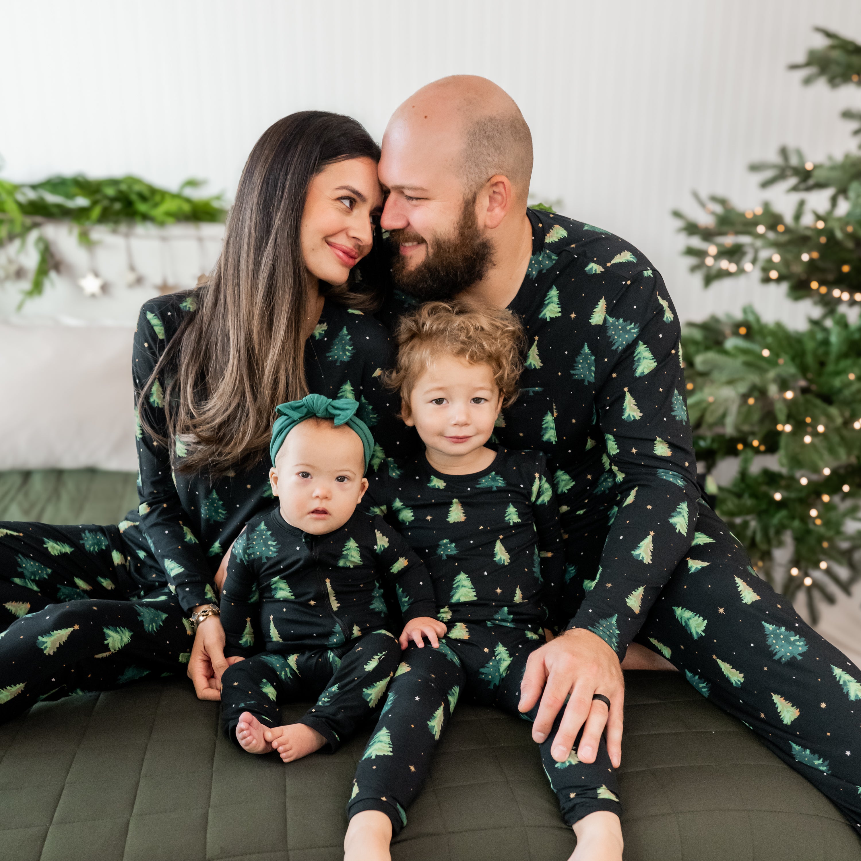 Family of four sitting on a bed wearing matching pajamas in the  Twinkle Tree print