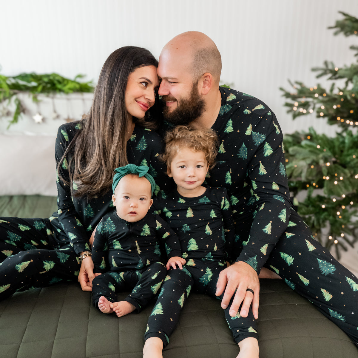 Family of four sitting on a bed wearing matching pajamas in the  Twinkle Tree print