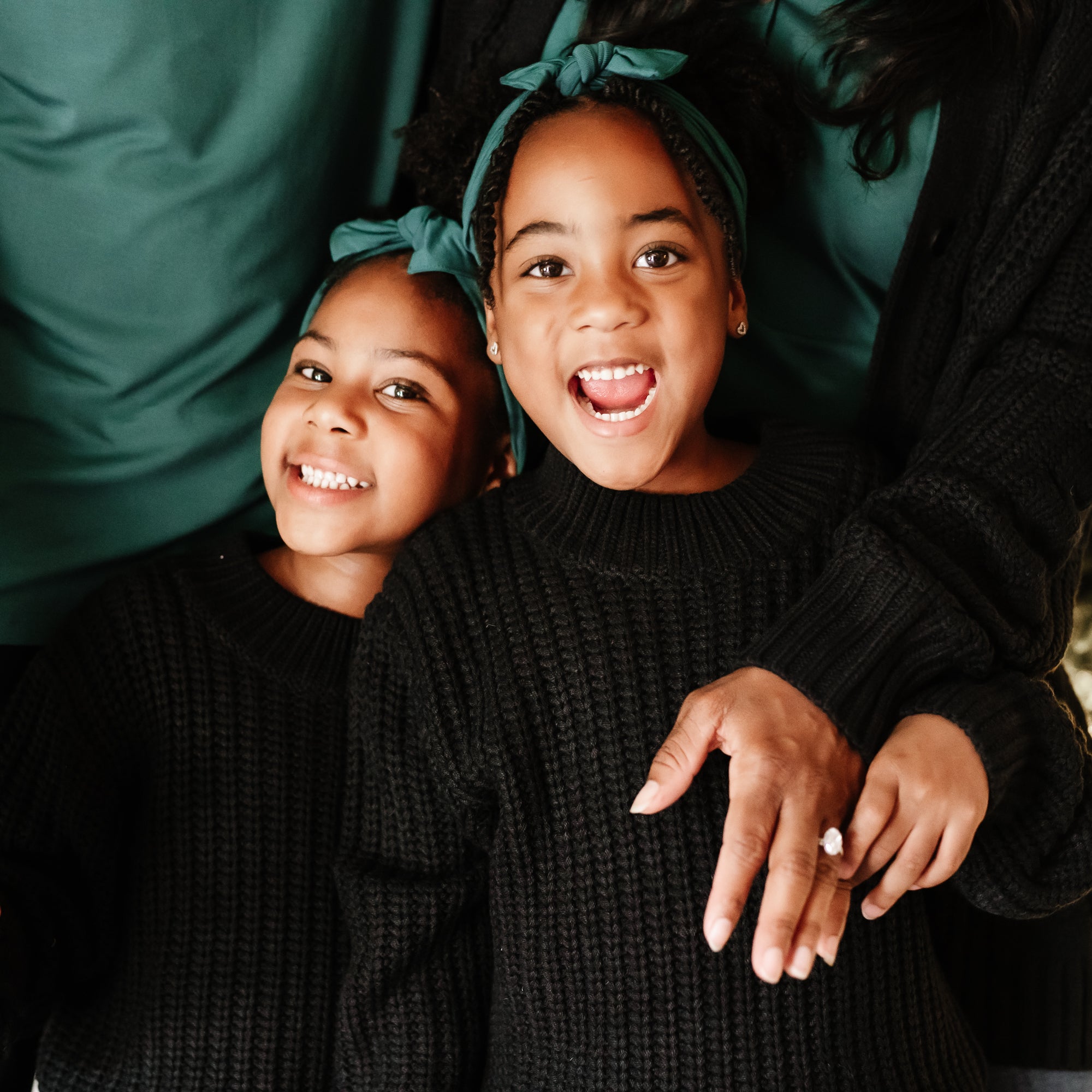 Sisters standing side by side wearing the Chunky Knit Sweater in Midnight with Green knotted bow headbands