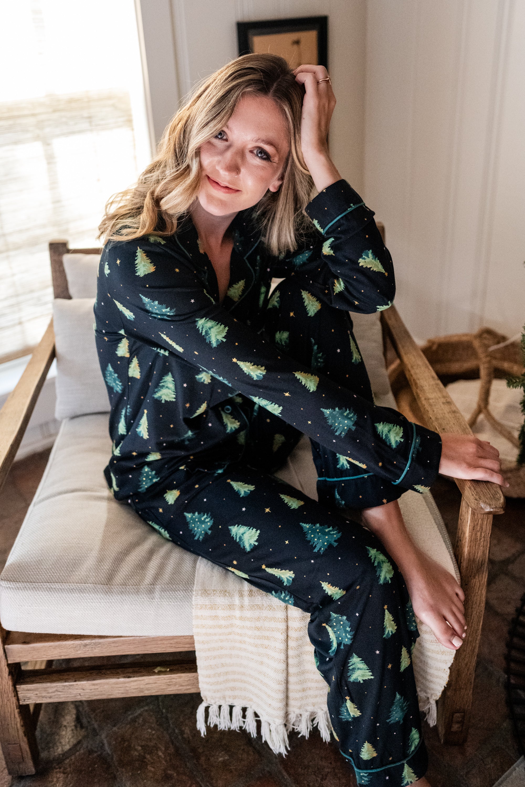 Female model sitting on a wooden chair wearing the Long-Sleeved Women's Pajama Set in Twinkle Tree