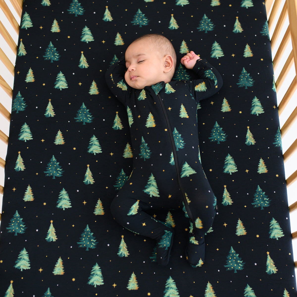 Sleeping infant laying in a crib on a Crib Sheet in Twinkle Tree wearing a matching zippered footie