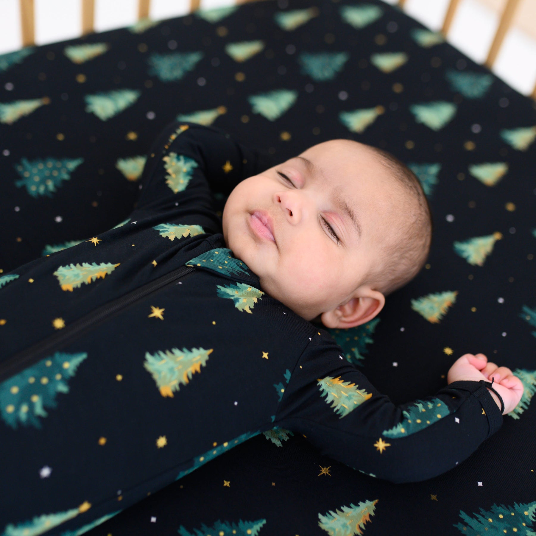 Close up of a sleeping infant laying on a Crib Sheet in Twinkle Tree and matching zippered footie
