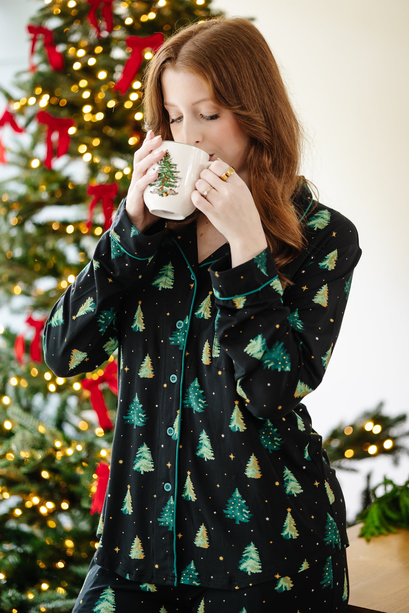 Female model wearing the Long-Sleeved Women's Pajama Set in Twinkle Tree drinking coffee from a Christmas tree mug