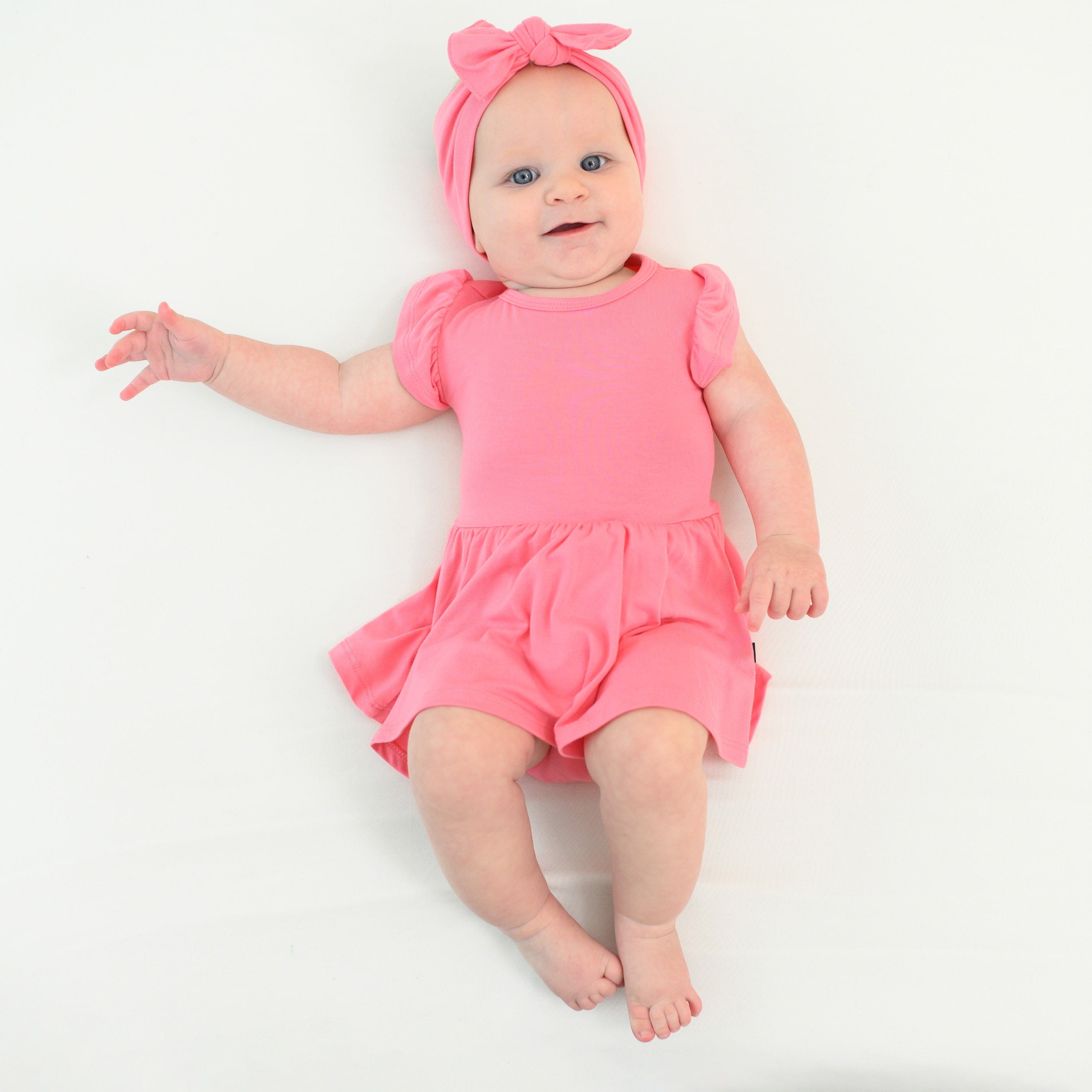 baby wearing twirl bodysuit dress and bow in guava