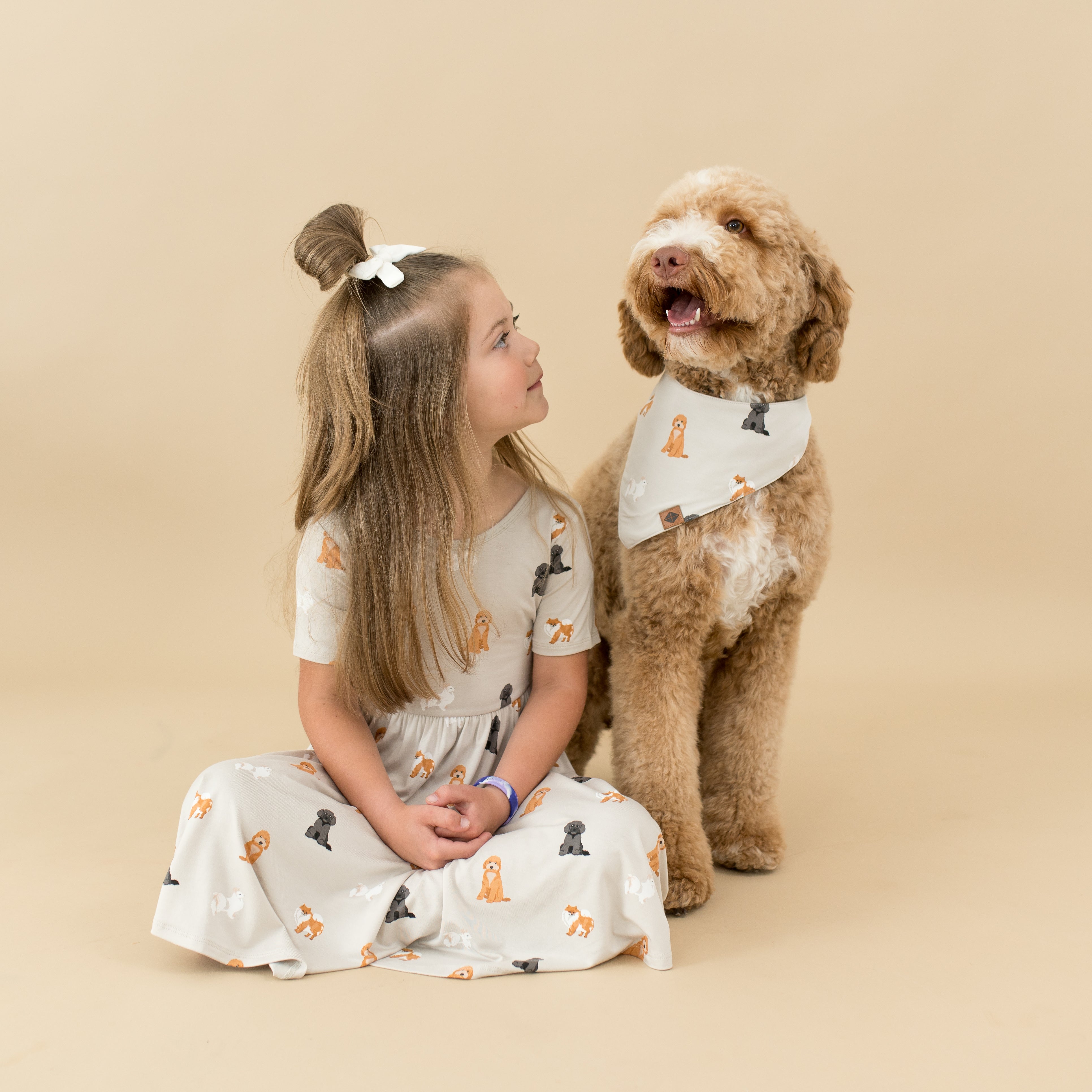Young girl sitting wearing the Fluffy Dog Twirl dress sitting beside her dog who is wearing a matching dog bandana