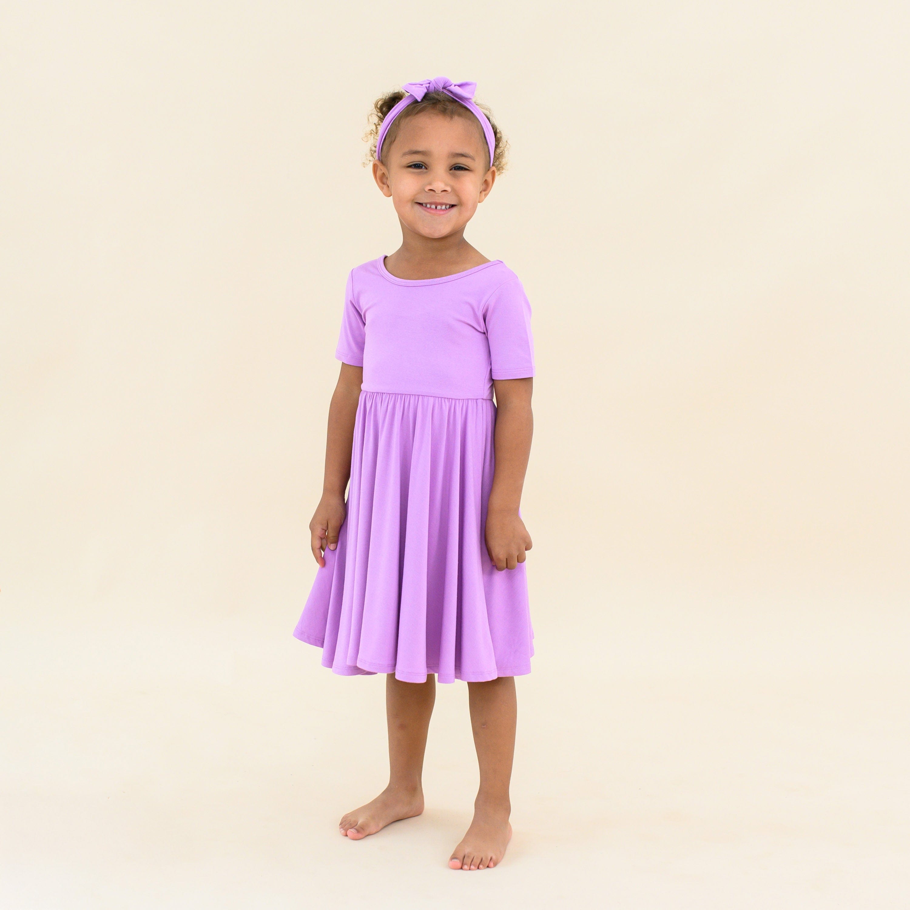 toddler wearing in kyte baby twirl dress in poi with matching bow