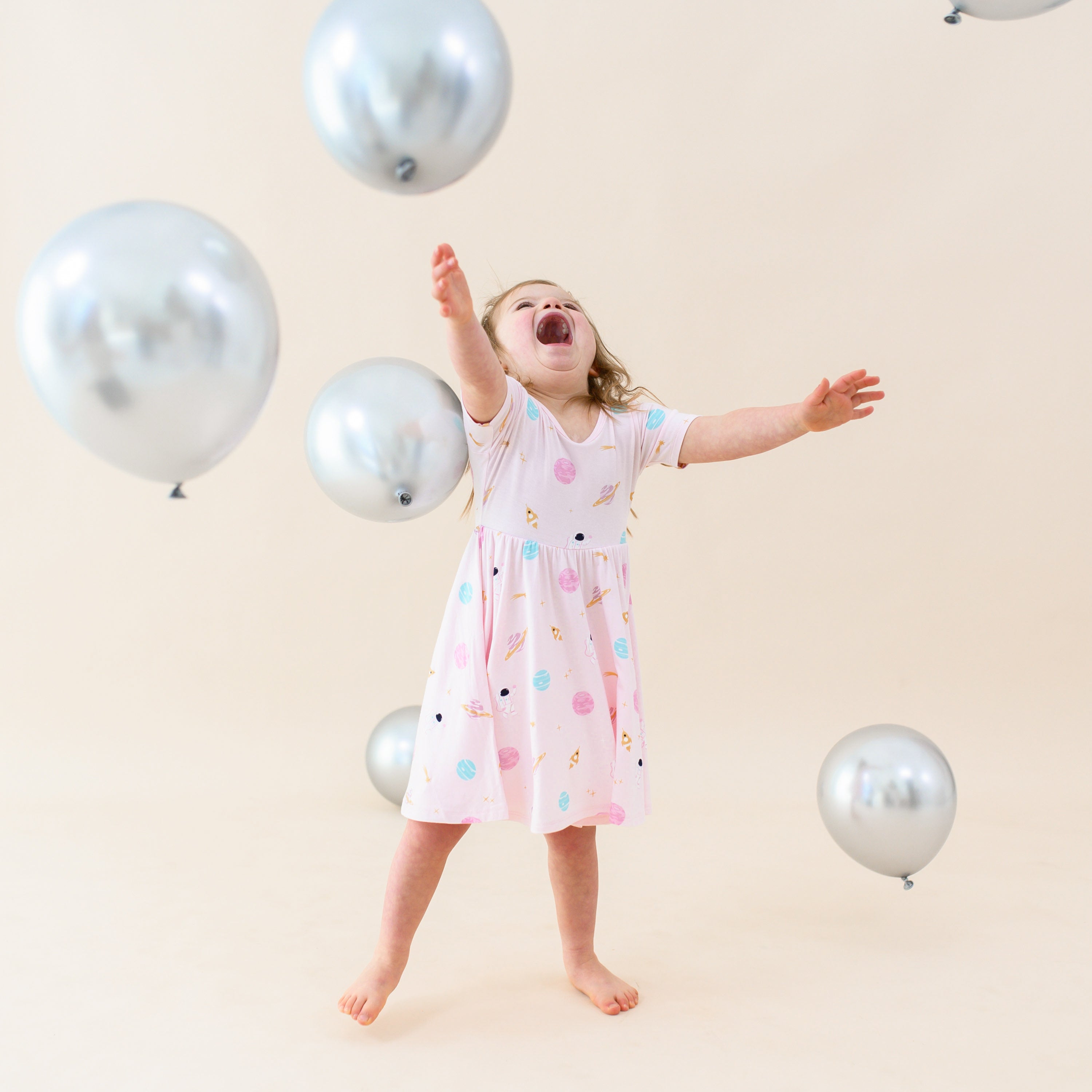 toddler wearing sakura space twirl dress playing with silver balloons