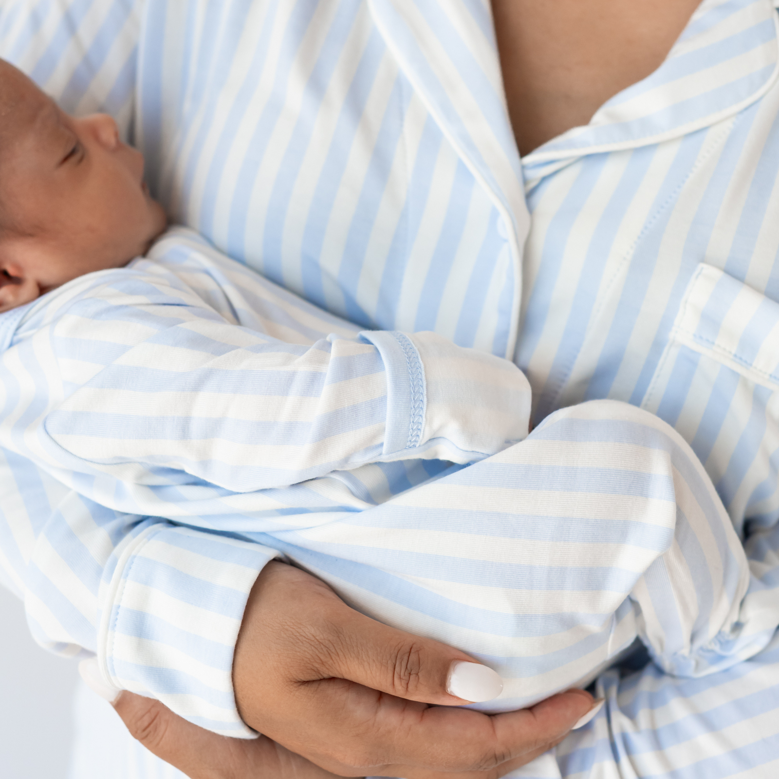 Mom in mist stripe pajama set holding baby in matching footie