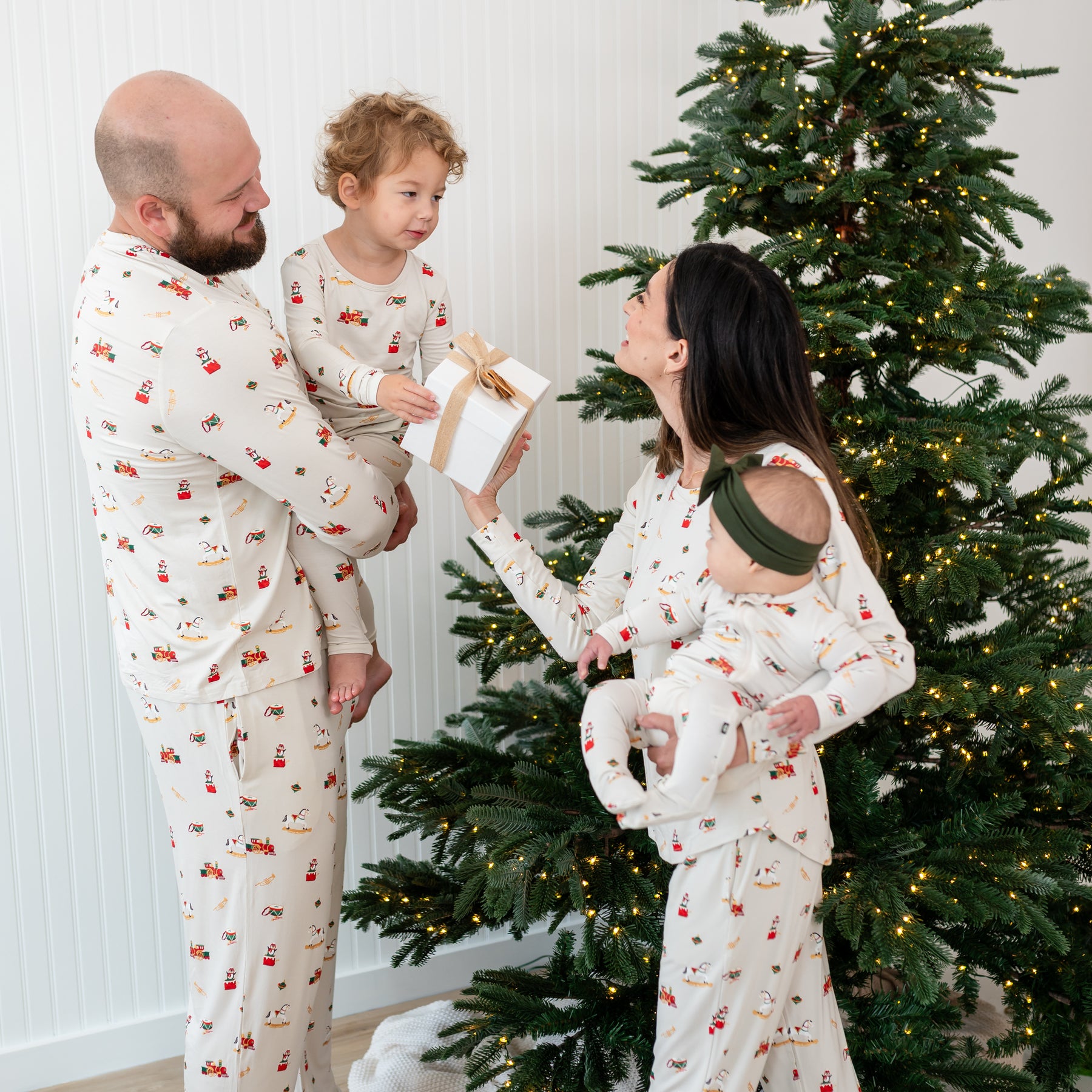 Family of four standing in front of a lit Christmas Tree wearing matching Vintage Toys Pajamas