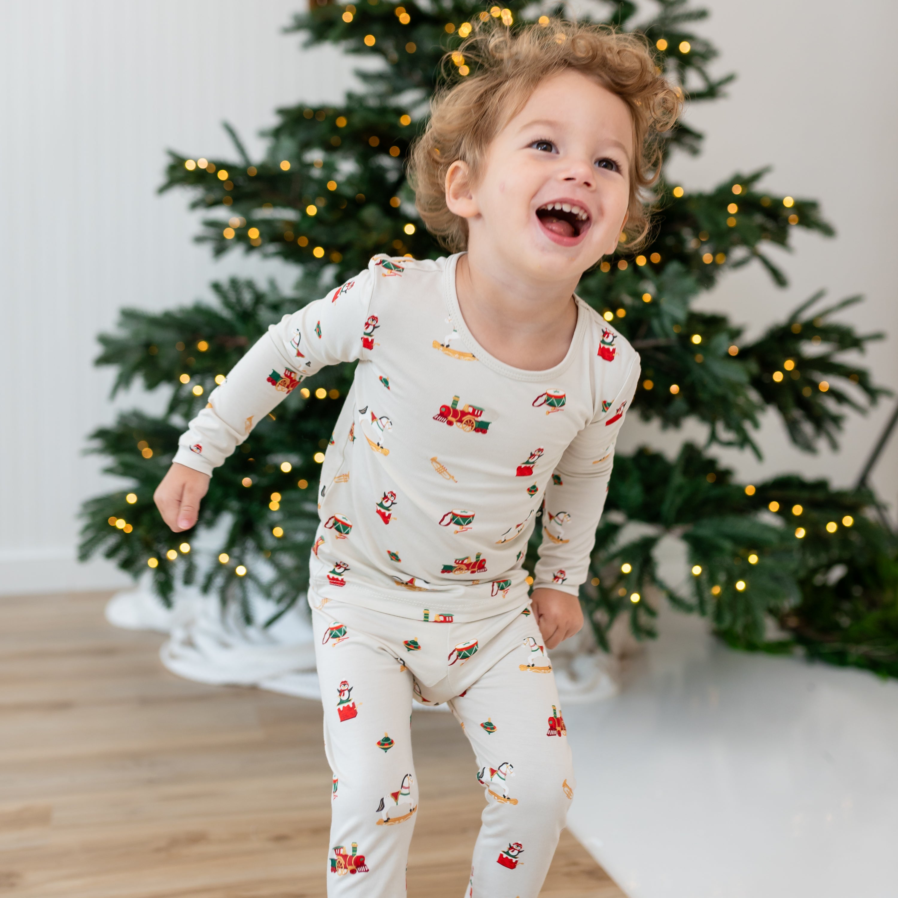 Laughing boy standing in front of  a Christmas tree wearing the Long Sleeve Pajamas in Vintage Toys