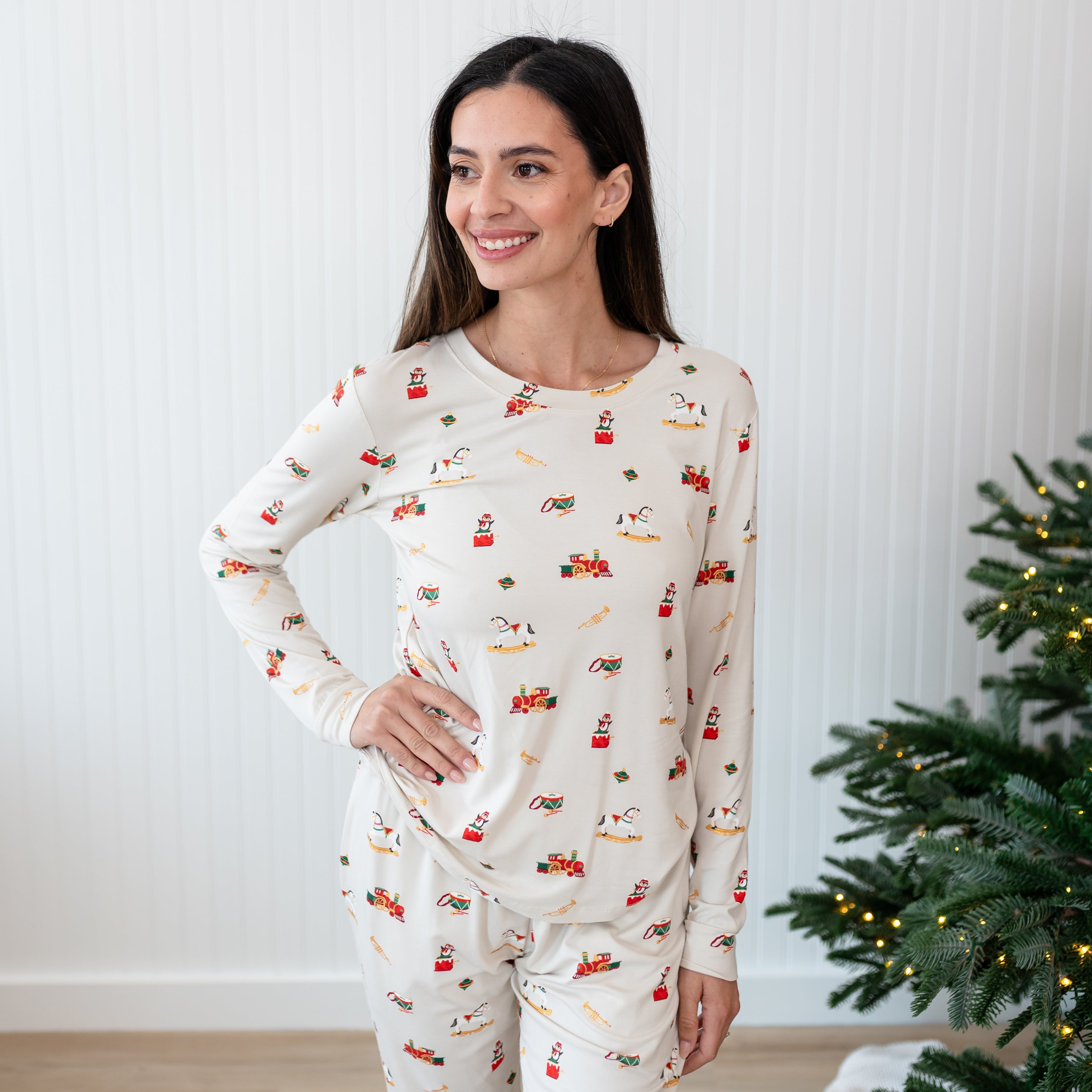 Female model standing with one hand on her hip in front of a white paneled wall wearing the Women's Jogger Pajama Set in Vintage Toys