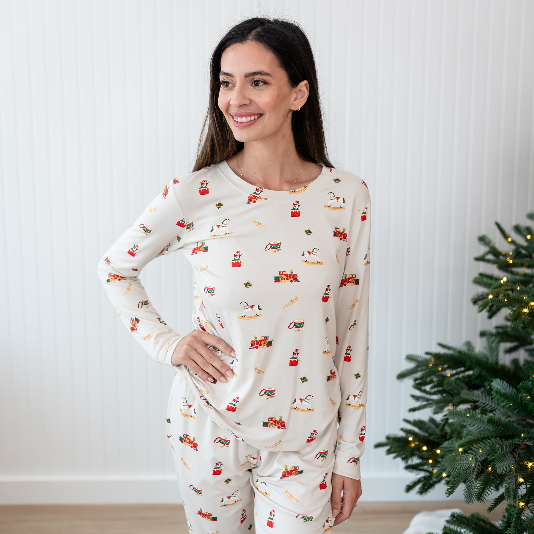 Female model standing with one hand on her hip in front of a white paneled wall wearing the Women's Jogger Pajama Set in Vintage Toys