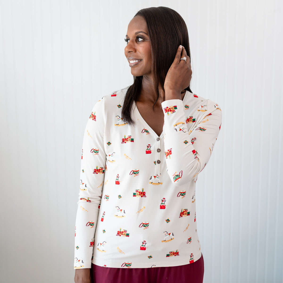 Close up of the Women's Long Sleeve Henley Tee in Vintage Toys shown on a female model standing in front of a white paneled wall