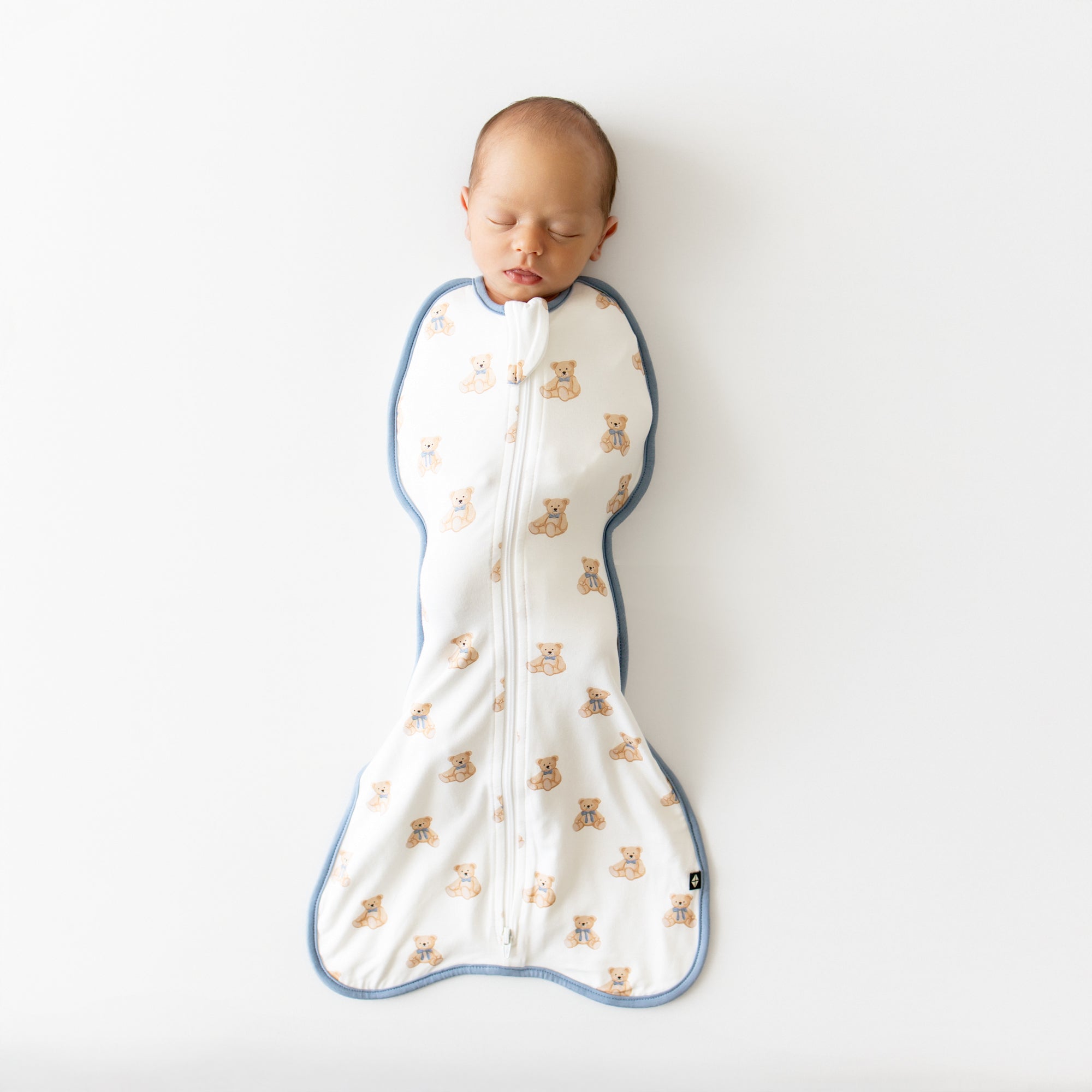 Baby sleeping in a white swaddle bag with teddy bear pattern on a white background