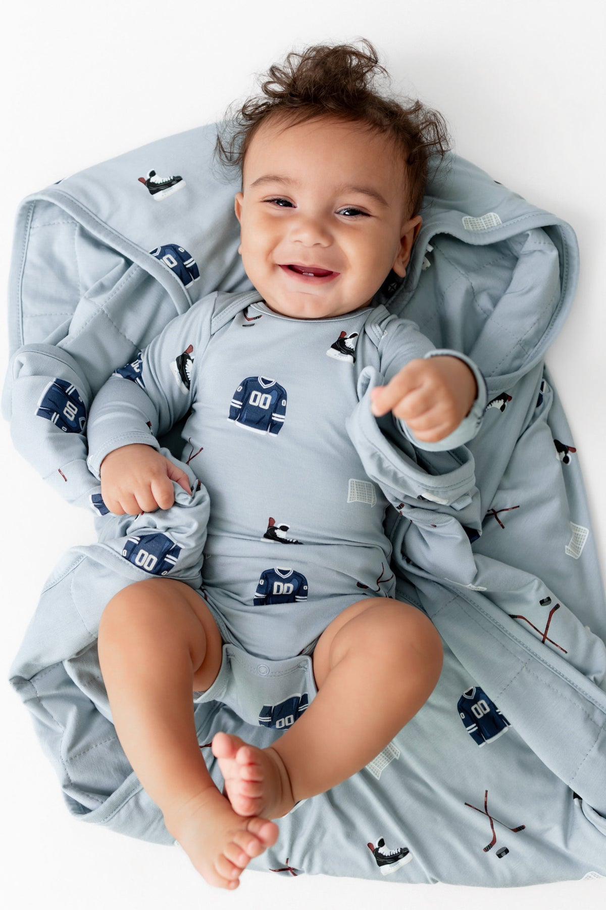 Baby lying over Baby Blanket in Vintage Hockey 1.0 print wearing a similar print bodysuit on a white background