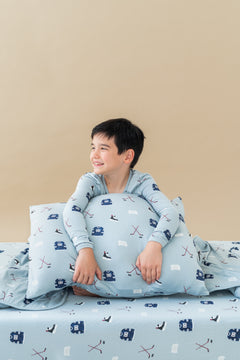 Boy holding Standard Pillowcase in Vintage Hockey print wearing a similar print long sleeve pajama set while sitting on a similar print sheets