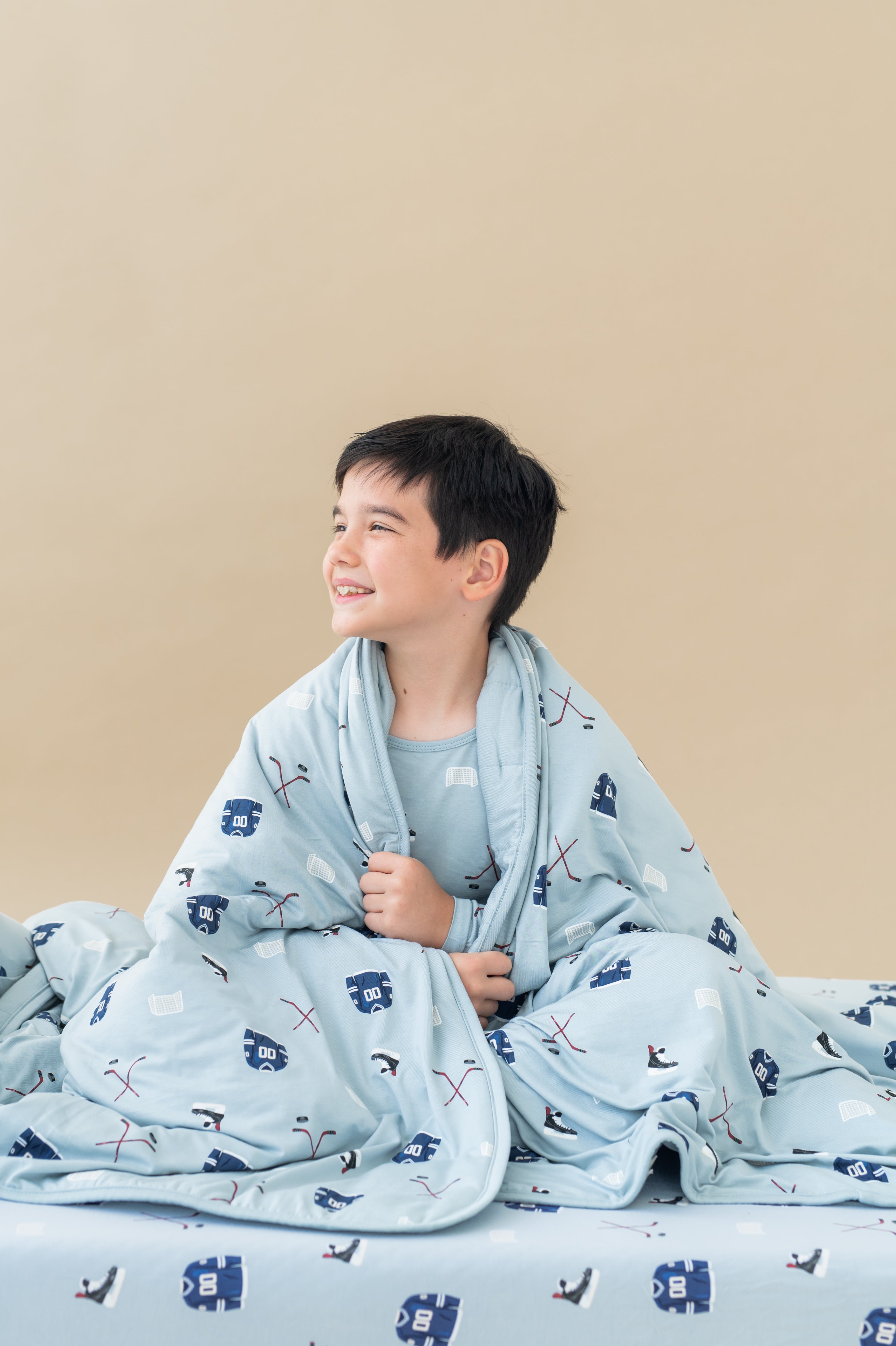 Boy posing with Youth Blanket in Vintage Hockey 2.5 print sitting on a similar print sheets on a beige background
