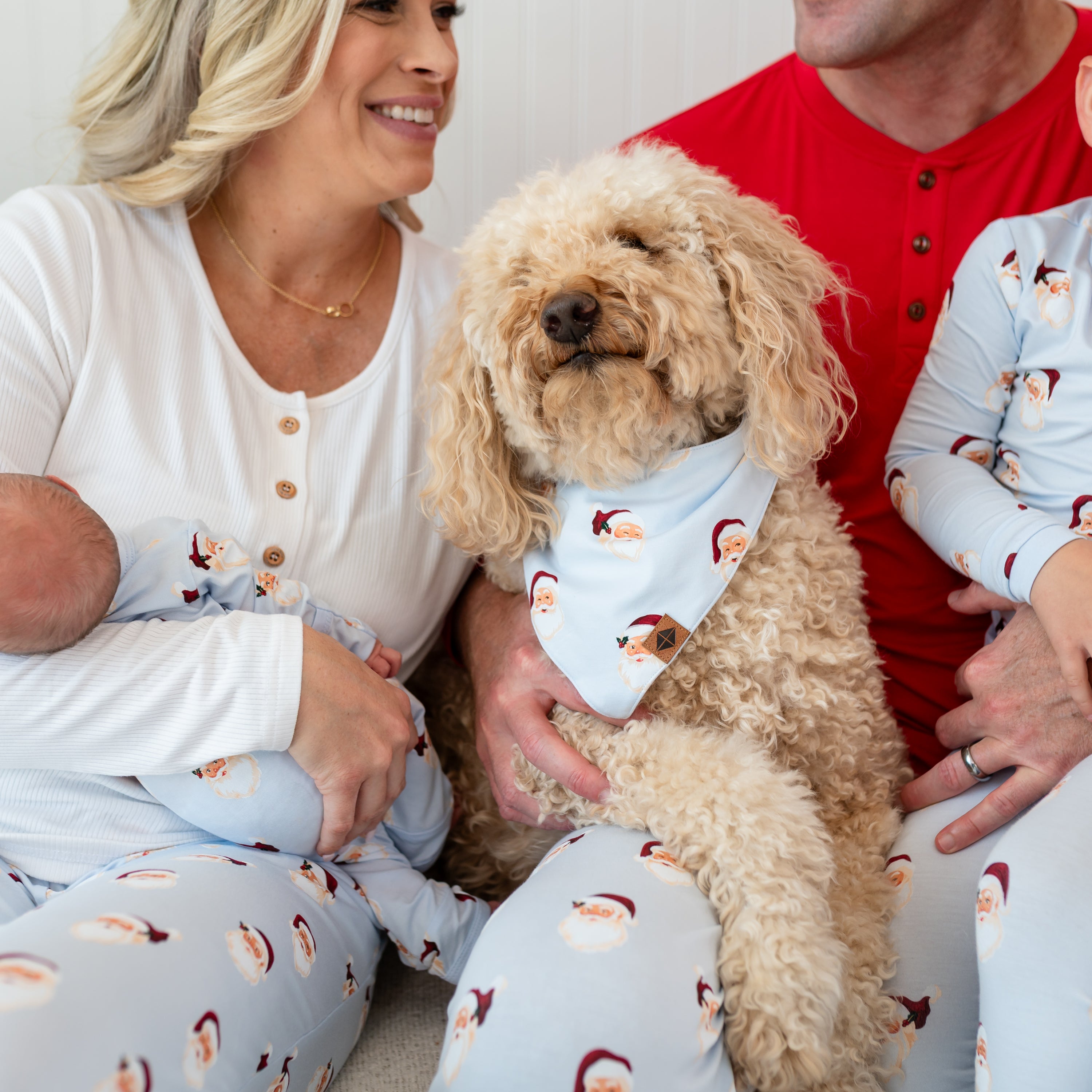 Family sitting on a cream ottoman with a medium sized dog in the center wearing the Dog Bandana in Vintage Santa