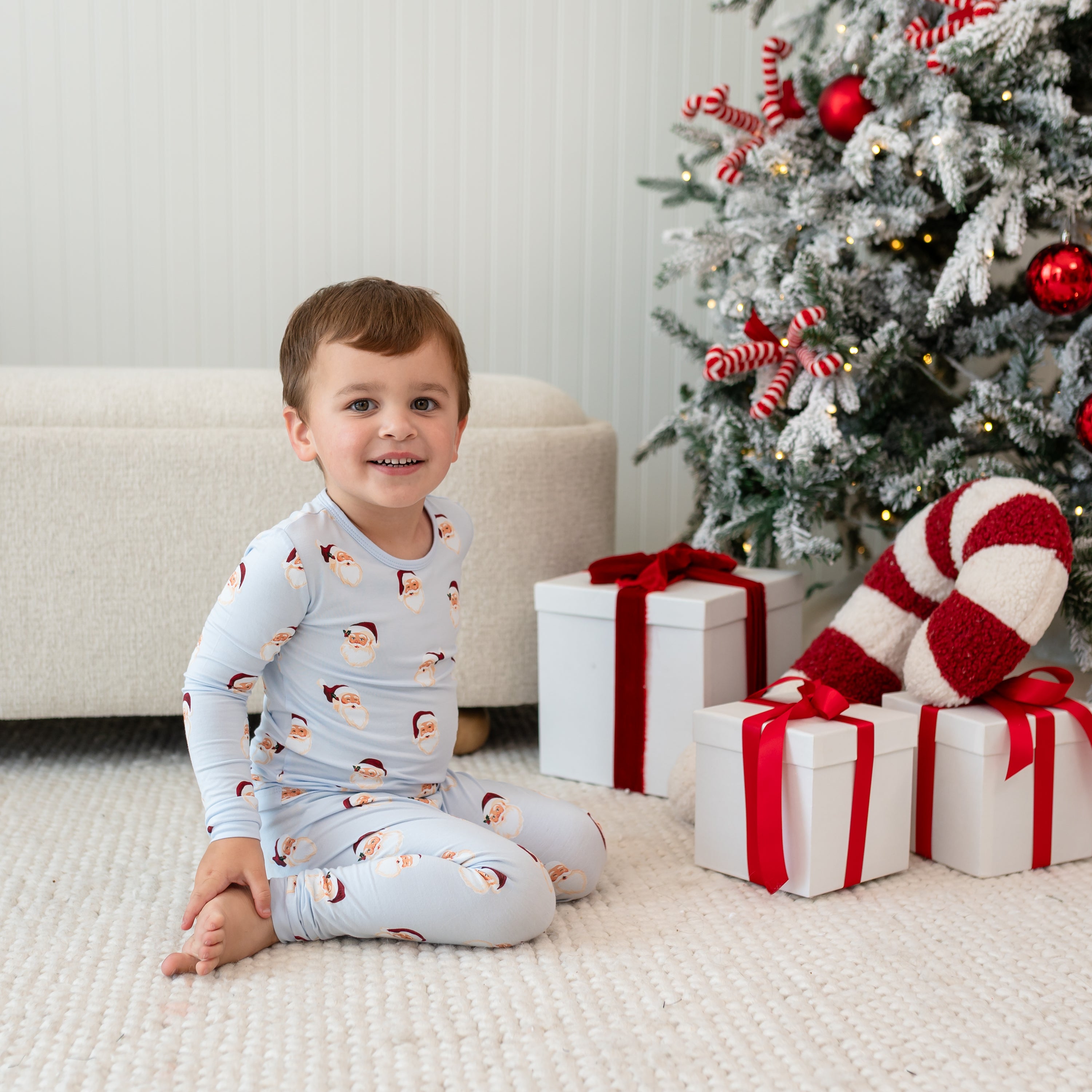 Young boy sitting on the floor in front of a decorated Christmas tree and gift boxes wearing the Long Sleeve Pajamas in Vintage Santa