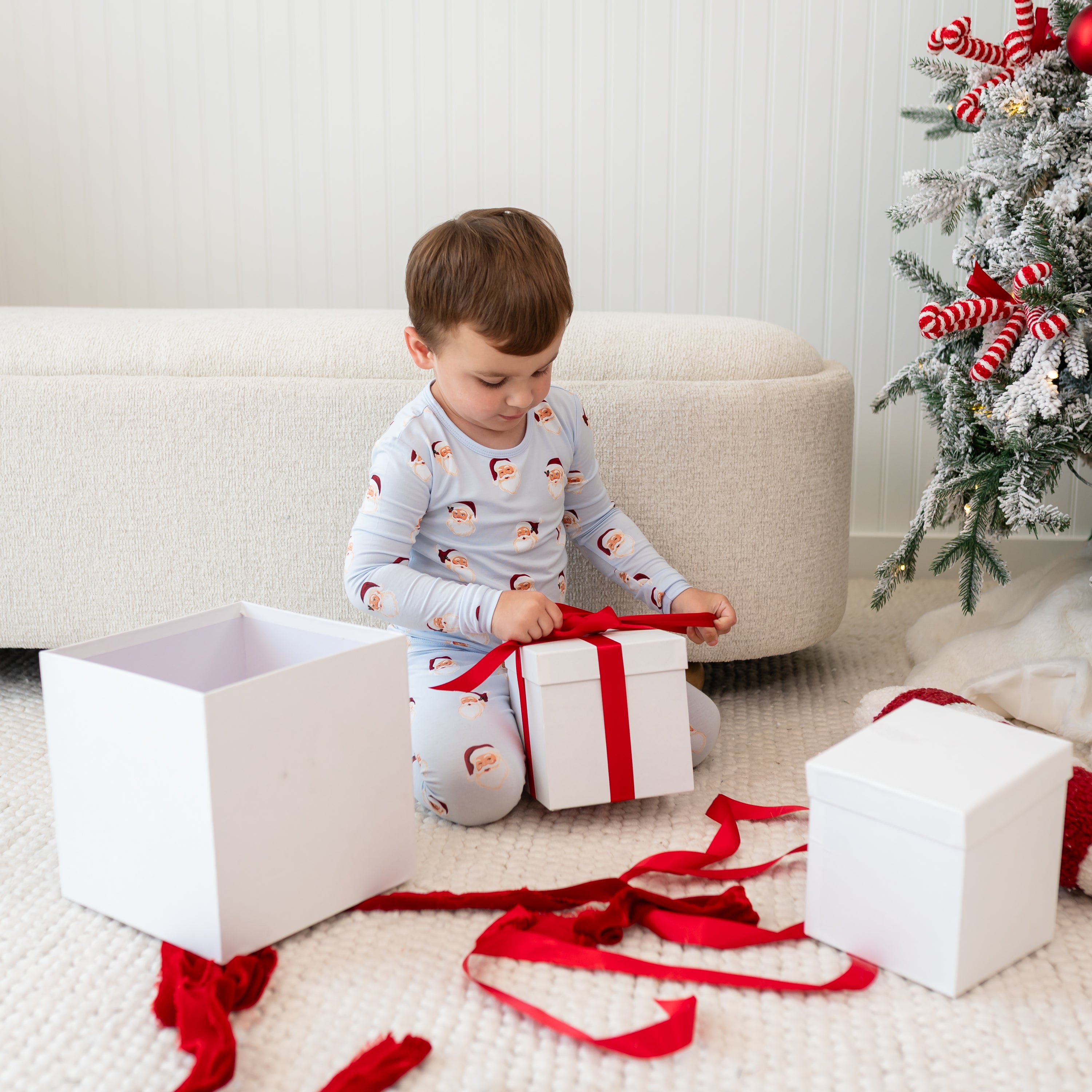 Young boy sitting on the floor unwrapping gift boxes wearing the Long Sleeve Pajamas in Vintage Santa