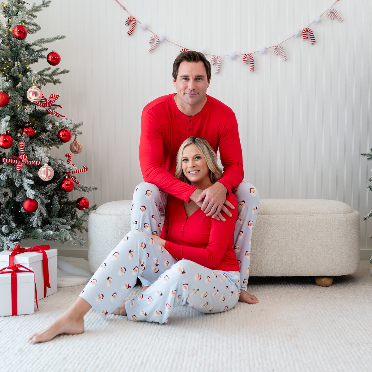 Husband wearing the Men's Lounge Pants in Vintage Santa and Cardinal Henley sitting on an ottoman with his wife in front of him matching in Vintage Santa Lounge pants and a Women's Cardinal Henley