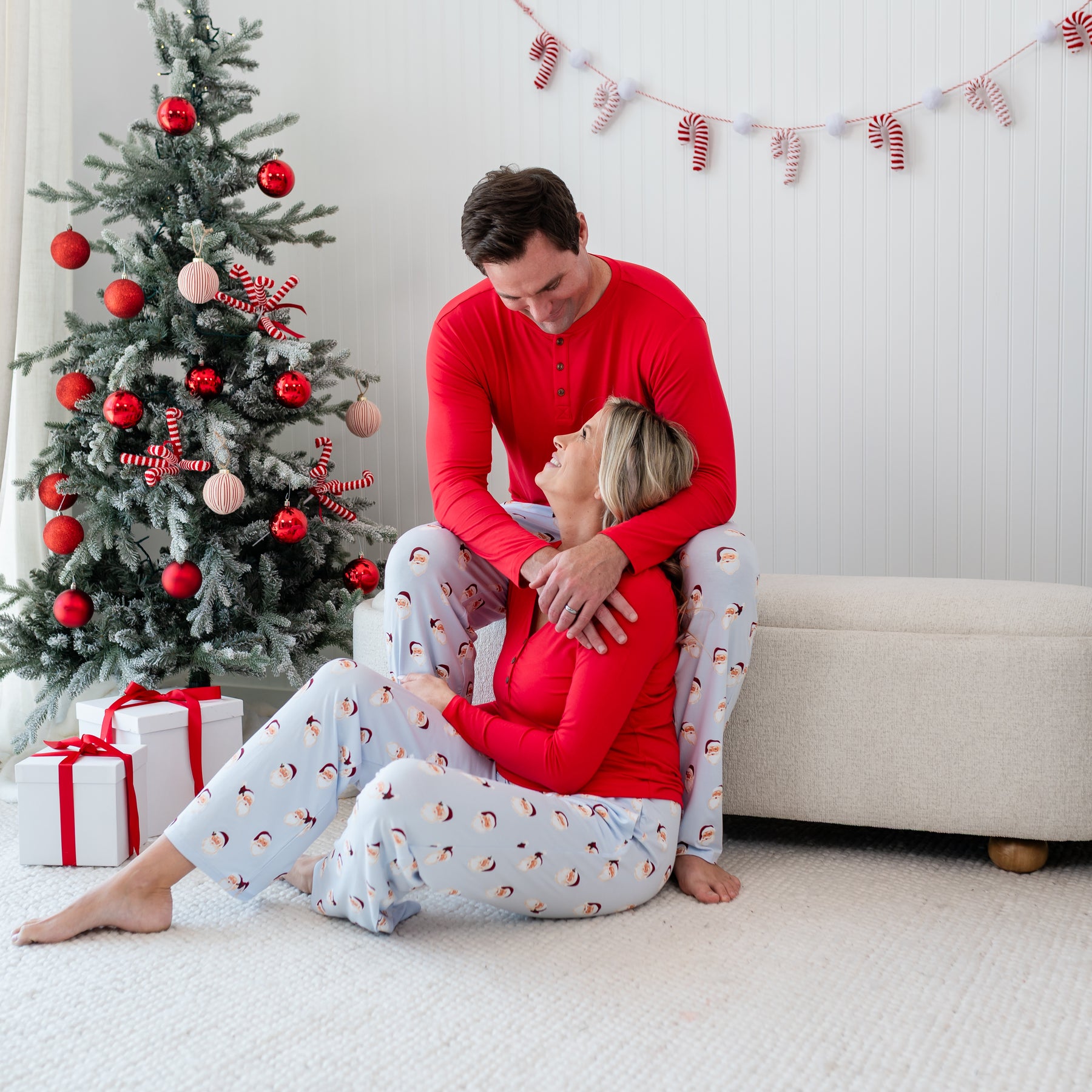 Husband and wife sitting down wearing matching Men's  and Women's Long Sleeve Henley Top in Cardinal and Vintage Santa Lounge pants