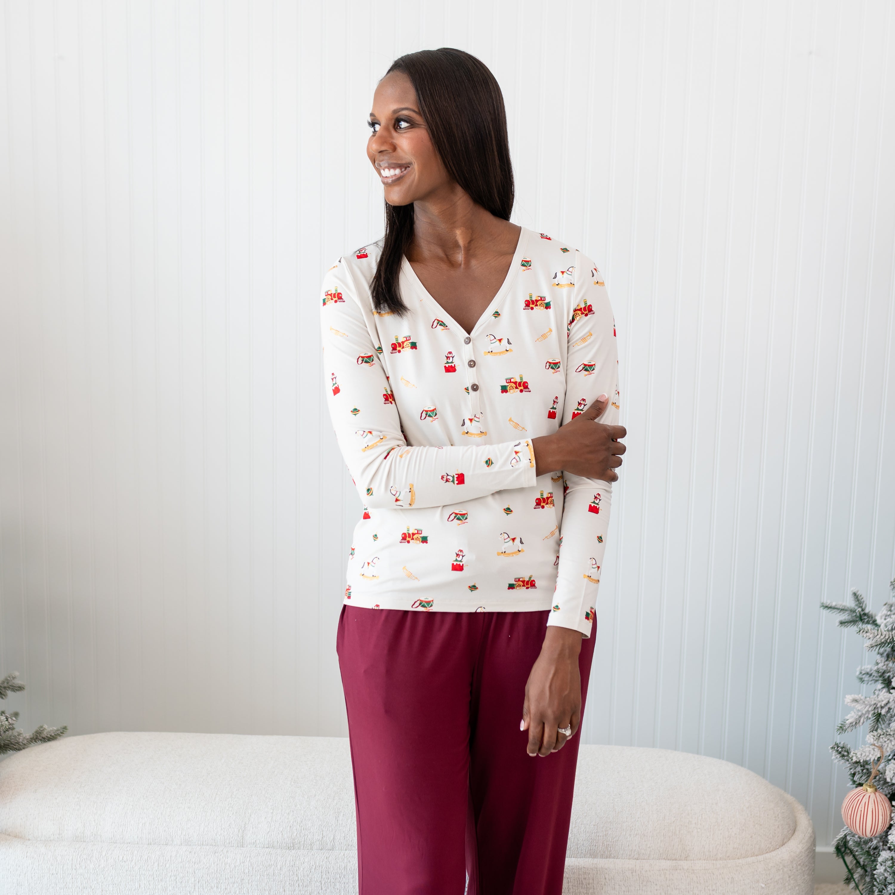 Female model standing in front of a white paneled wall posing wearing the Women's Long Sleeve Henley Tee in Vintage Toys