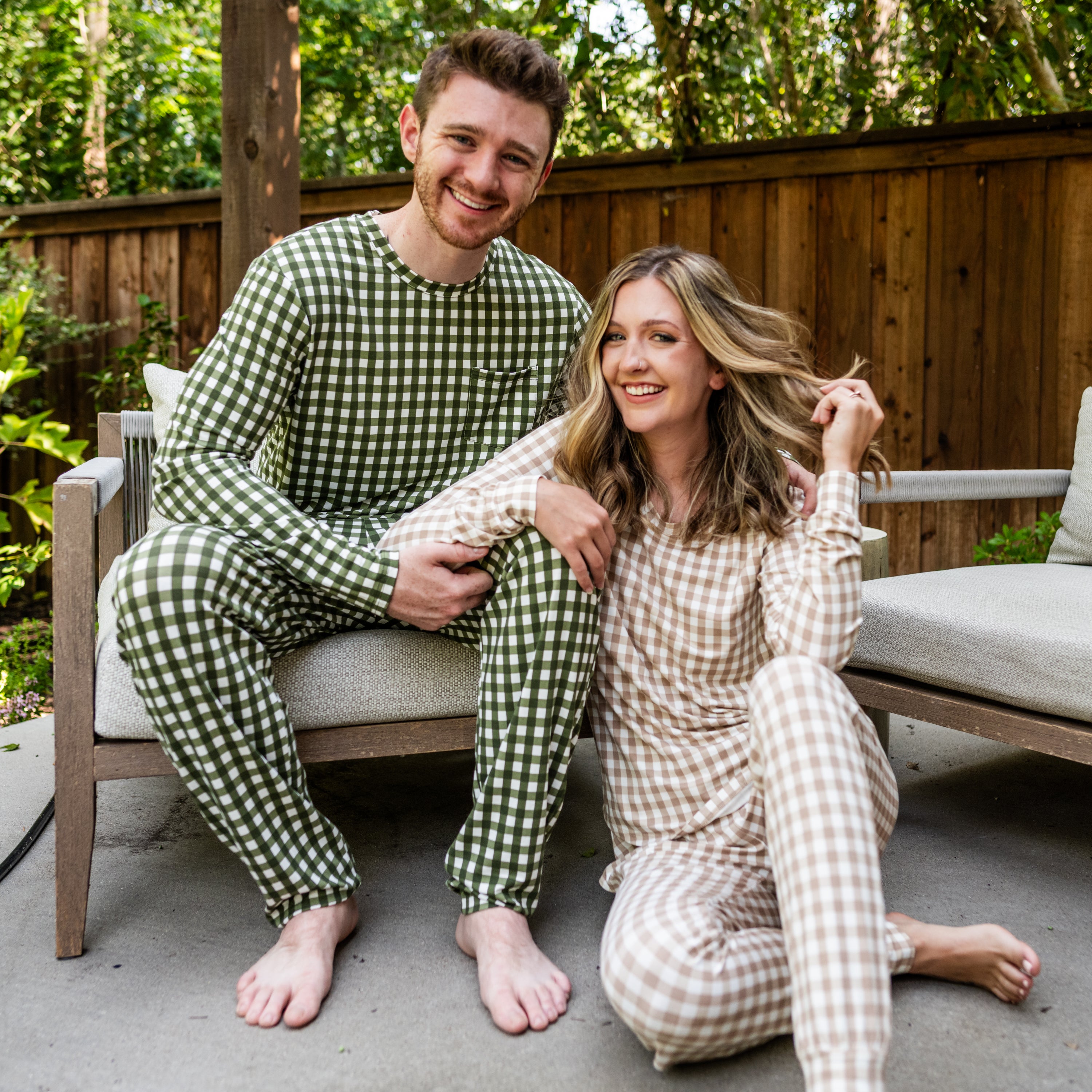 Husband and wife sitting side by side on patio chair. Husband wearing the Men's Jogger Set in Gingham Fir with the wife wearing the Women's Jogger Set in Gingham Bisque