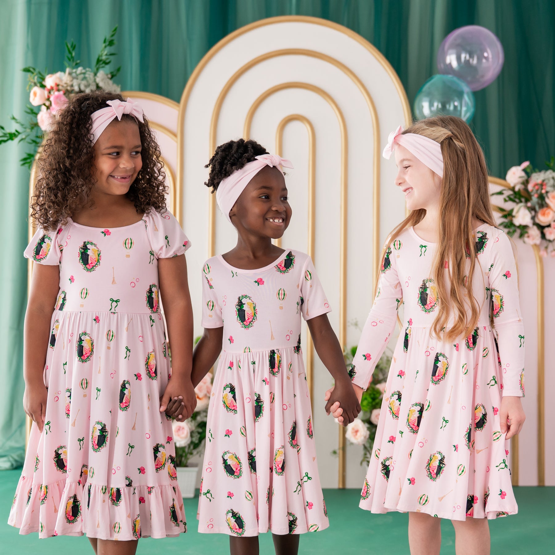 Three girls standing side by side holding hands wearing the Puff Sleeve Twirl dress, short sleeve twirl dress and long sleeve twirl dress in Wicked