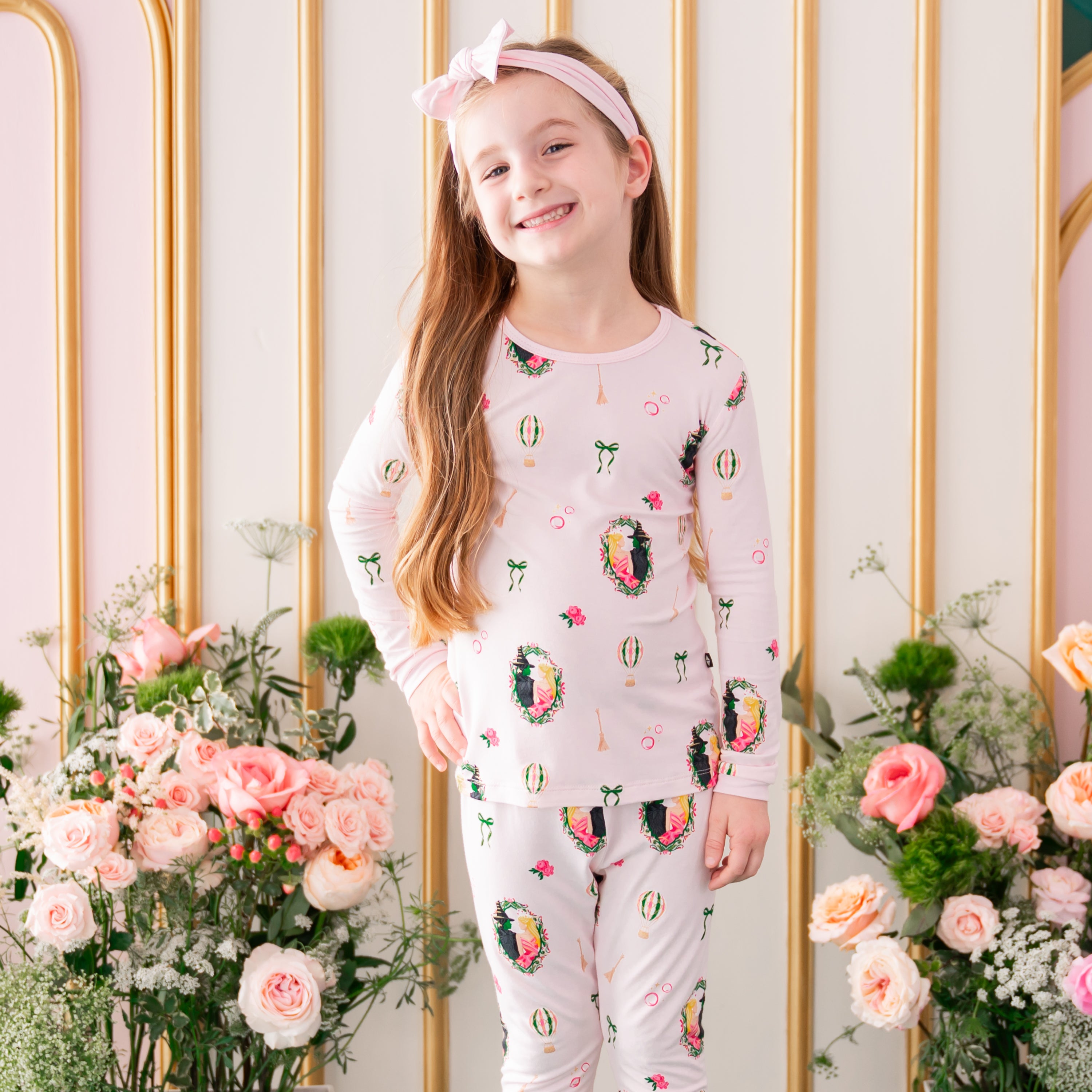 Close up of smiling girl wearing the soft Long Sleeve Pajamas in Wicked from Kyte Baby in front of a floral backdrop