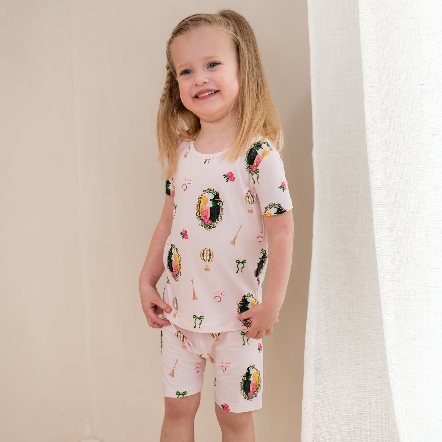 Young smiling girl standing in front of a light beige wall wearing the Short Sleeve Pajamas in Wicked