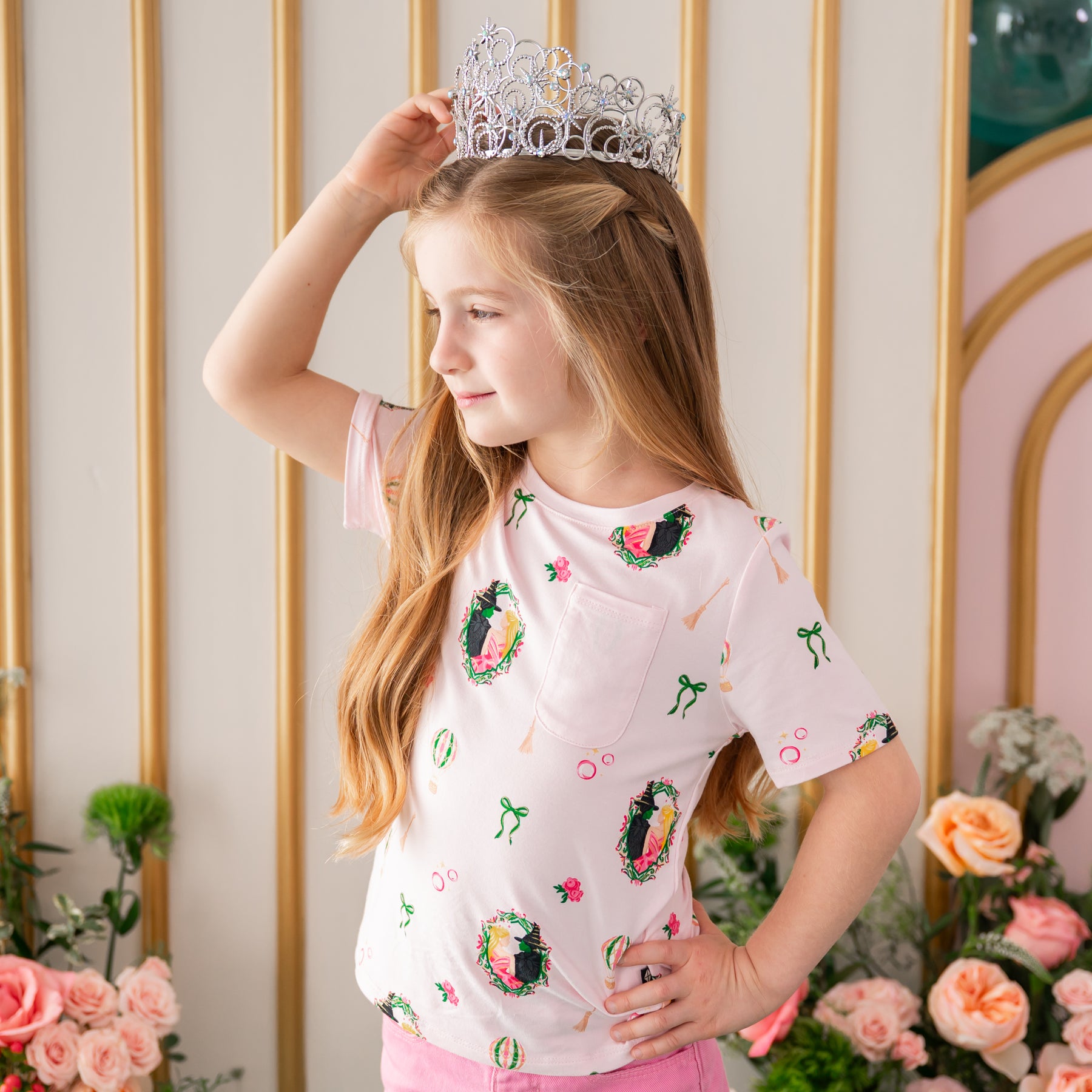 Girl posing wearing the Toddler Crew Neck Tee in Wicked with a prop tiara in front of a floral backdrop