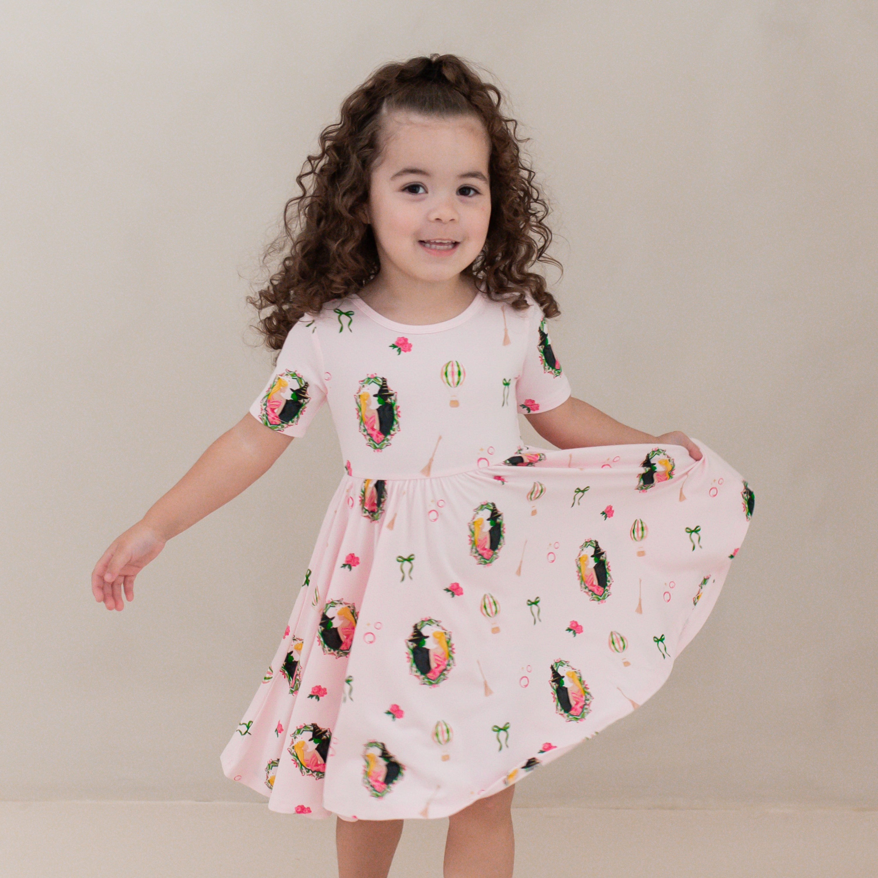 Young girl standing in front of a beige neutral background wearing the breathable and flowy Twirl Dress in Wicked from Kyte Bbay