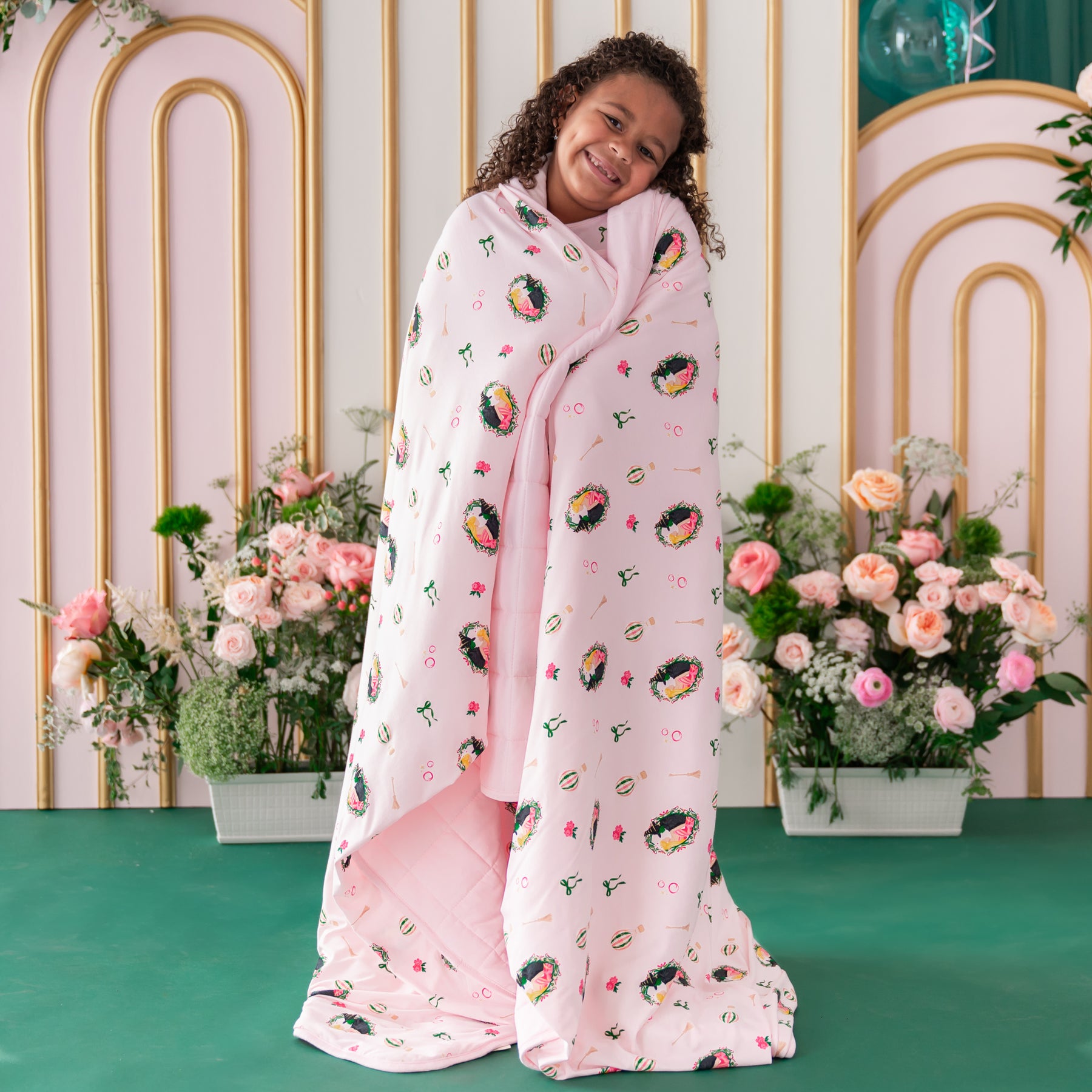 Girl standing in front of a floral backdrop with the soft and cozy Youth Blanket in Wicked 2.5 around her shoulders